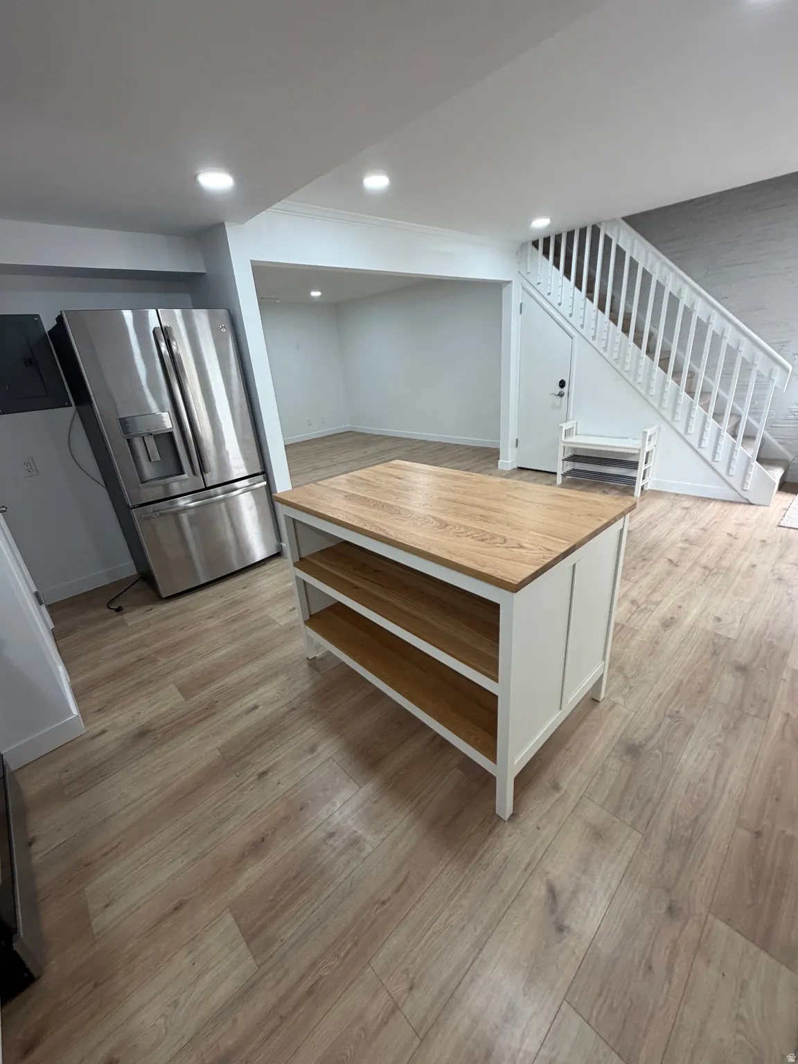 Open-concept living area featuring wood-finish flooring, recessed lighting, and a prominent staircase with white railings