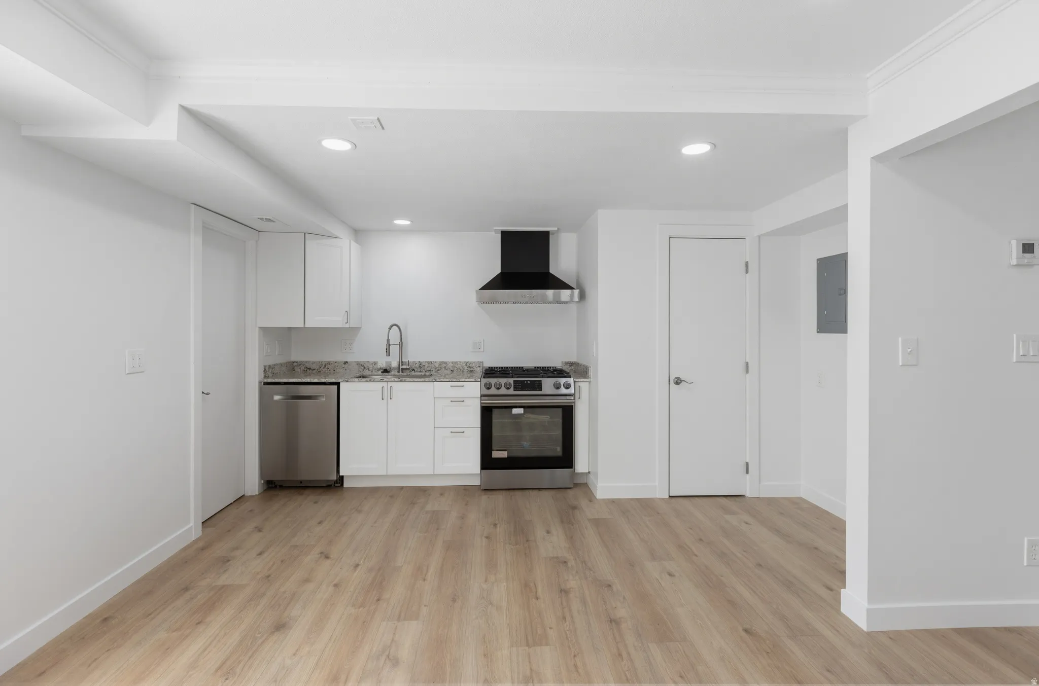 Kitchen featuring stainless steel appliances, white cabinets, light wood-style floors, light stone countertops, and recessed lighting