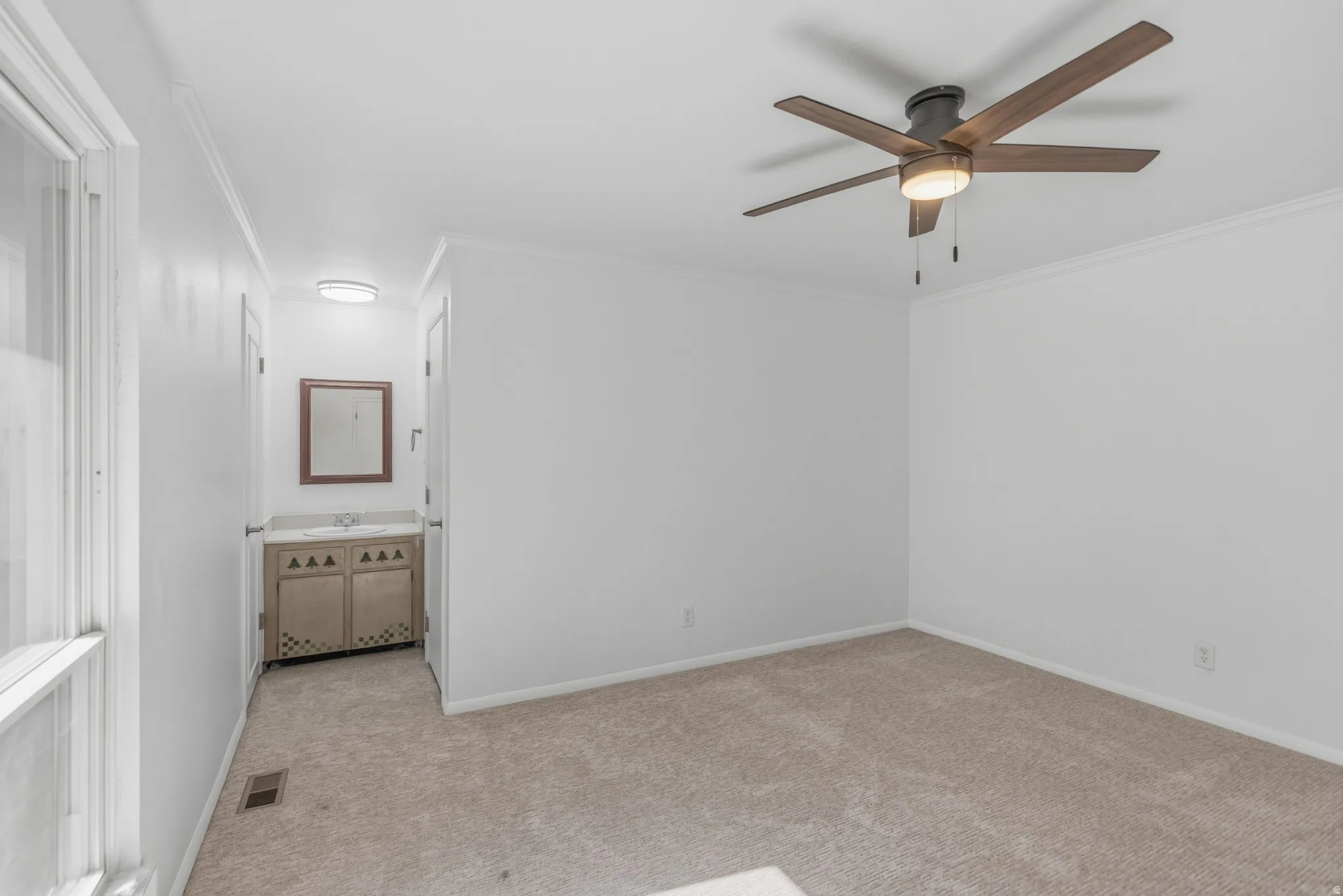 Unfurnished bedroom featuring crown molding, light colored carpet, a ceiling fan, and ensuite bath