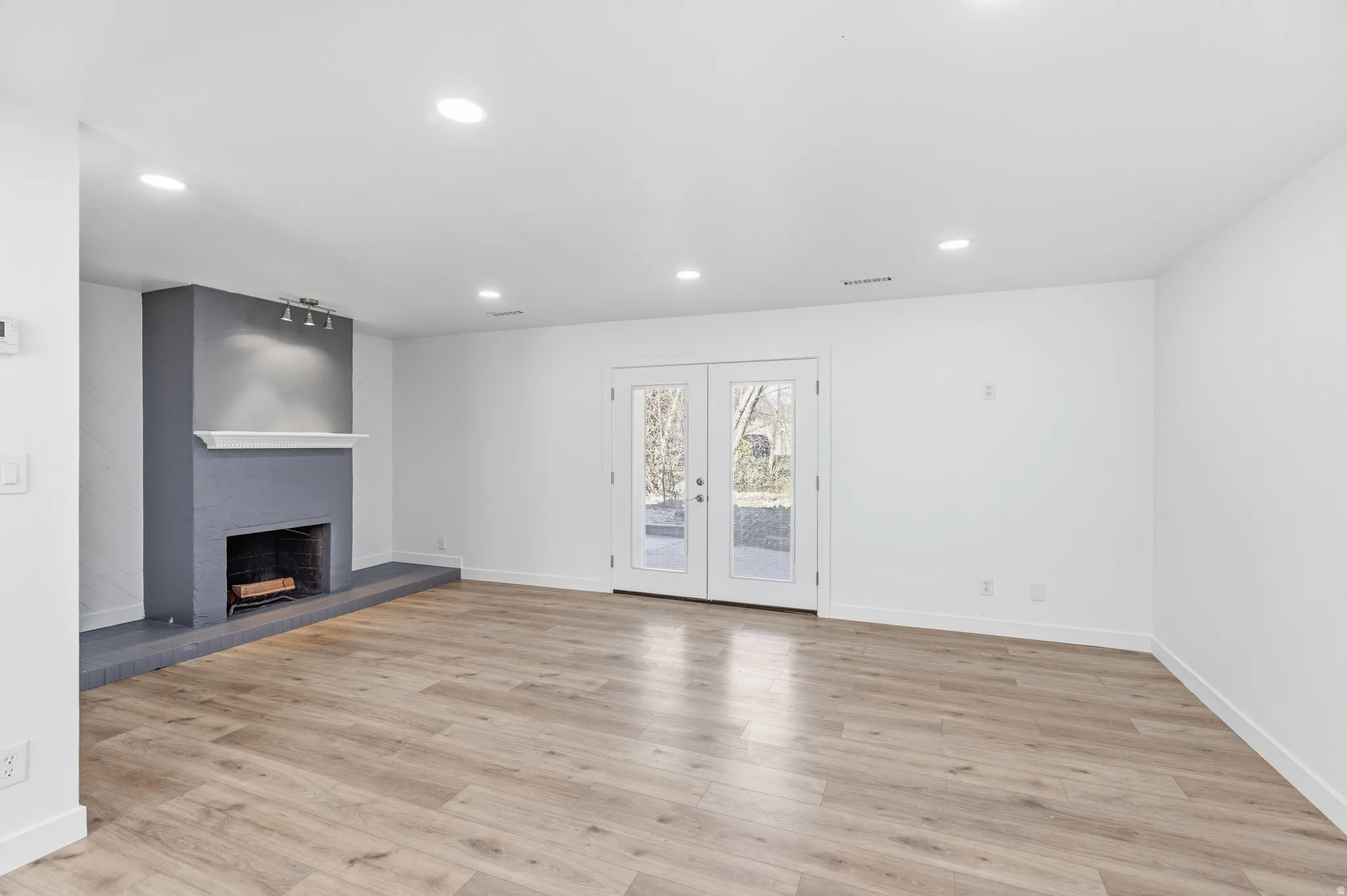 Unfurnished living room featuring french doors, recessed lighting, a fireplace with raised hearth, and light wood-style floors