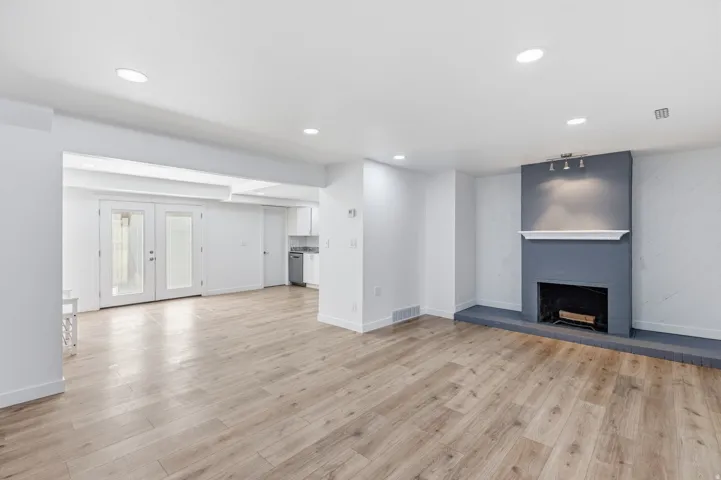 Unfurnished living room with a fireplace with raised hearth, recessed lighting, french doors, and light wood-type flooring
