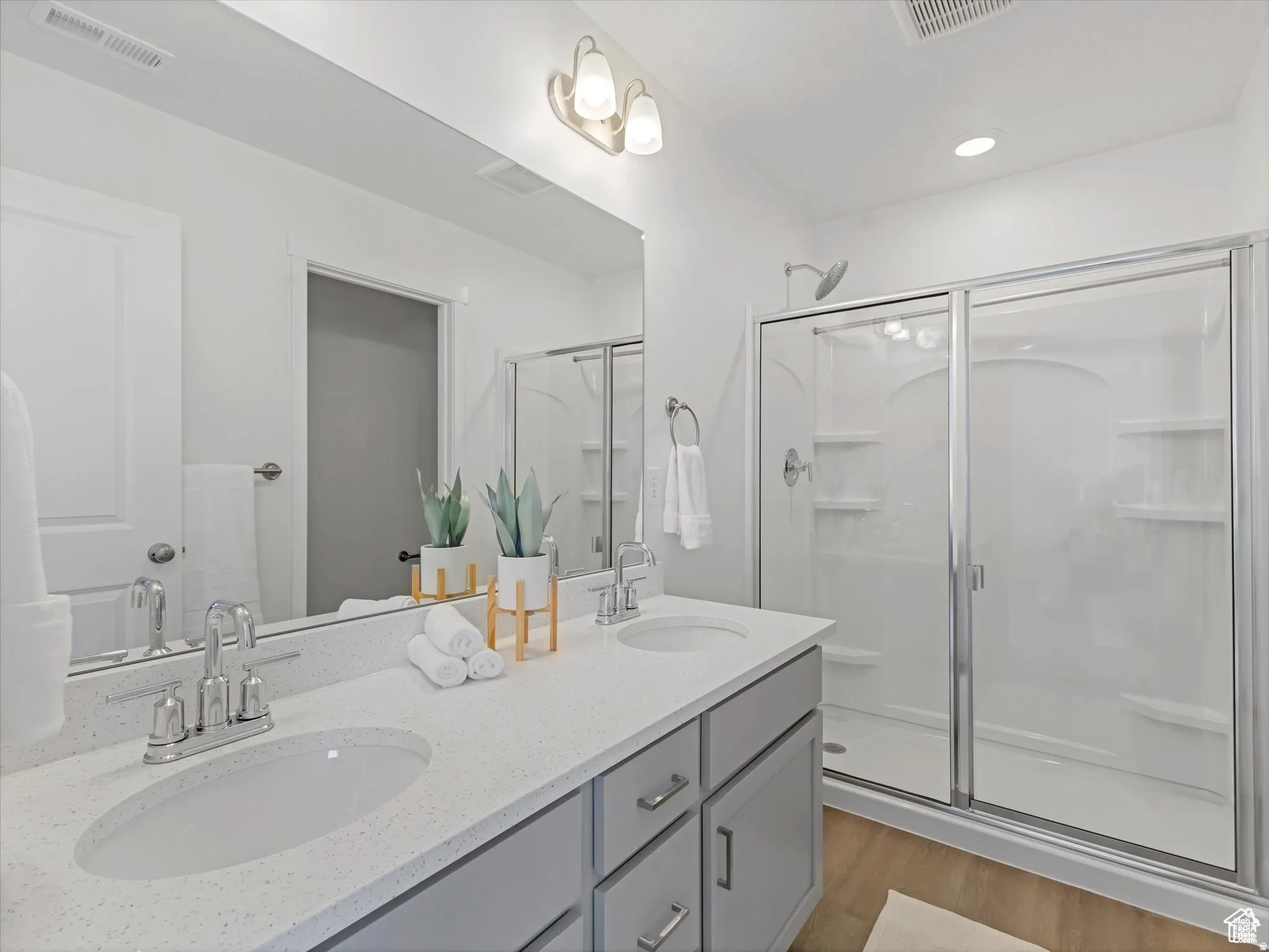 Full bath with double vanity, a stall shower, light wood finished floors, and recessed lighting