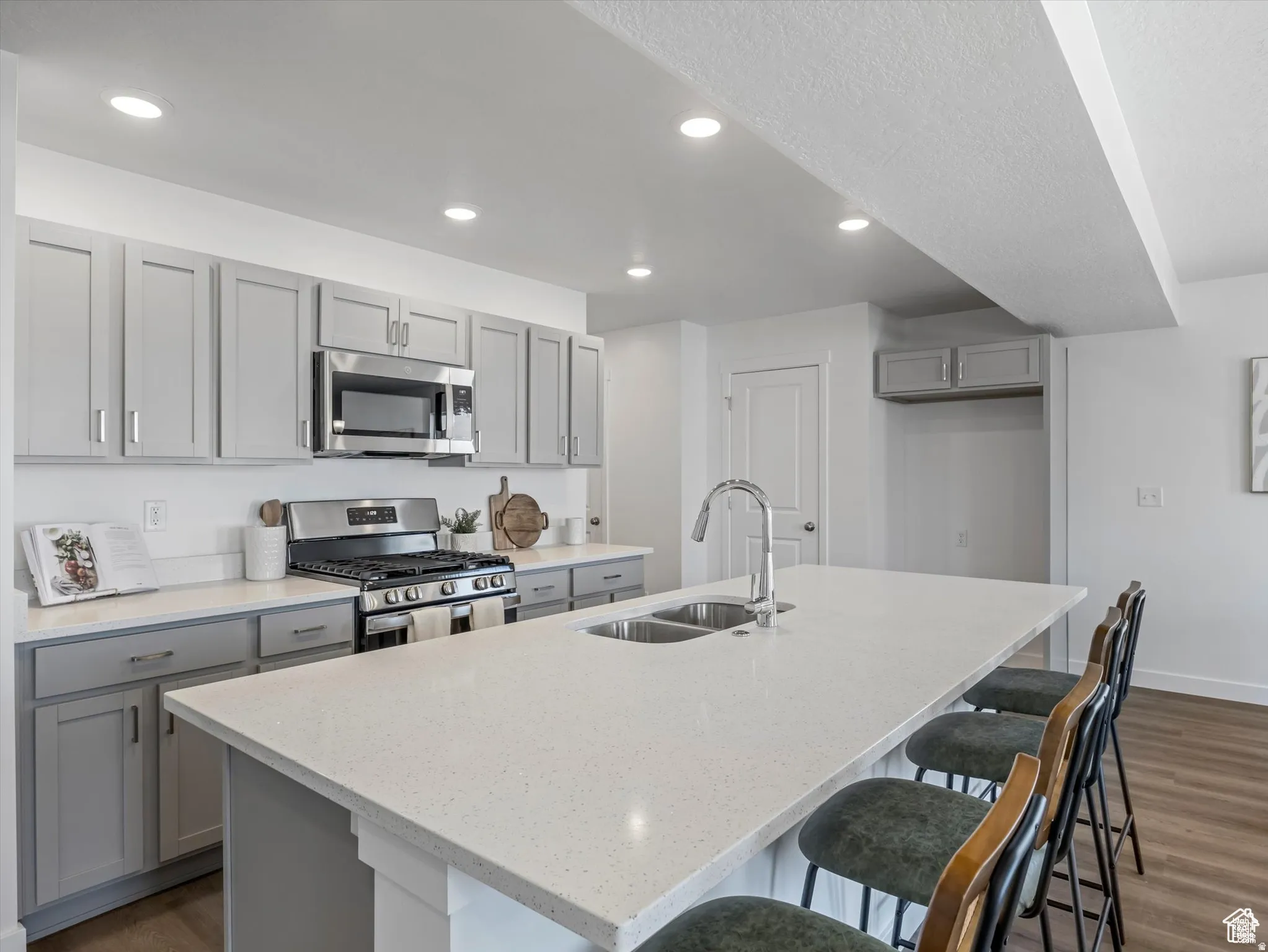 Kitchen with gray cabinetry, dark wood finished floors, stainless steel appliances, a breakfast bar area, and light stone countertops