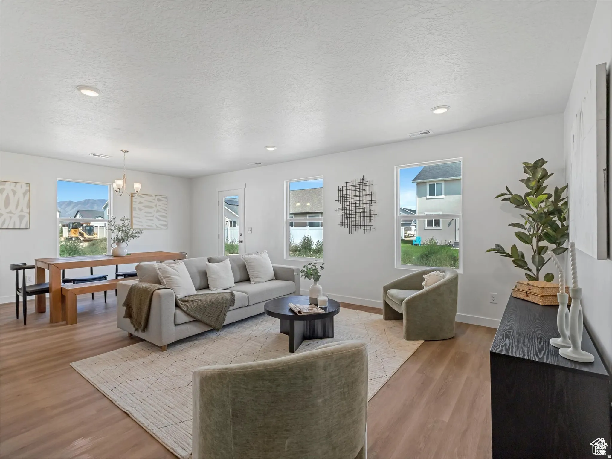 Living area with a textured ceiling, light wood finished floors, and suspended lighting
