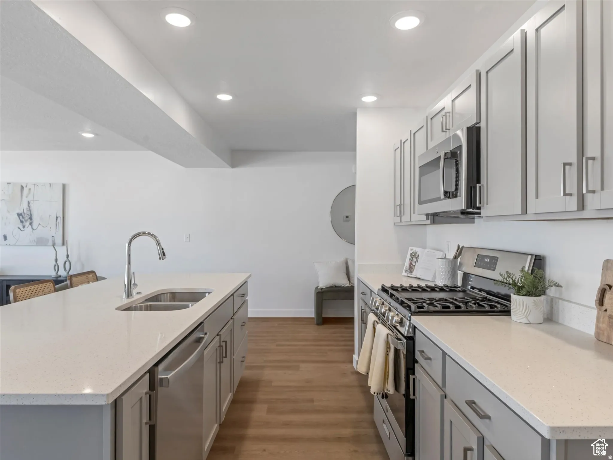 Two tone kitchen featuring stainless steel appliances, light stone counters, light wood-style floors, a center island with sink, and recessed lighting