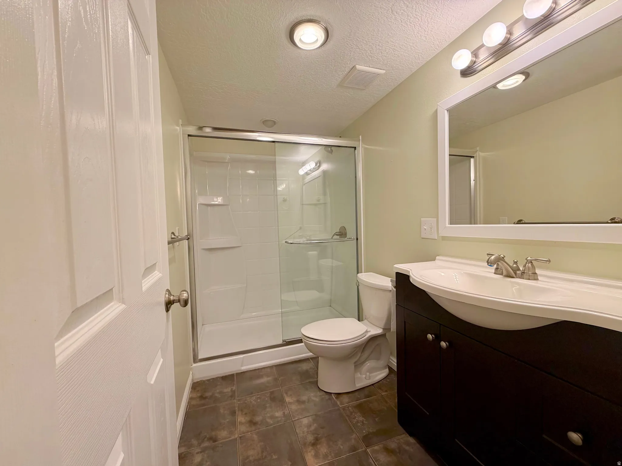 Bright full bath featuring vanity, a shower stall, and a textured ceiling