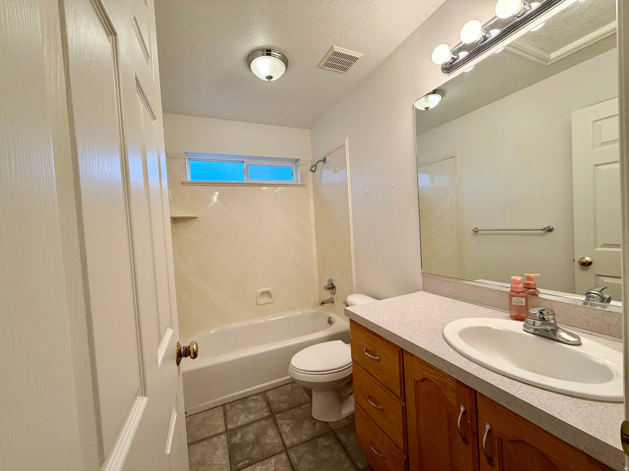 Bathroom with a textured ceiling, vanity, and bathing tub / shower combination conveniently located between the bedrooms