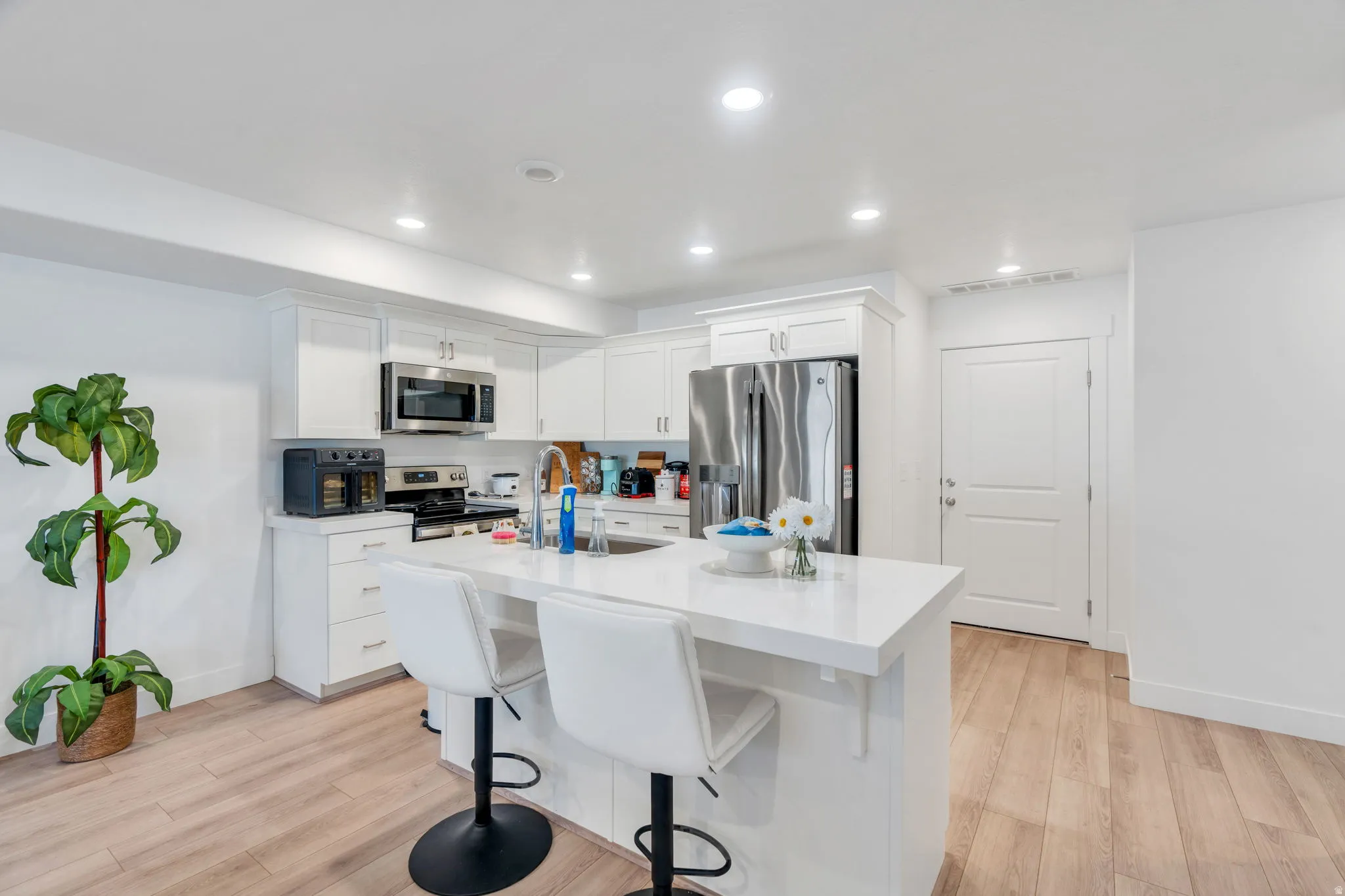 Kitchen featuring white cabinets, a kitchen bar, an island with sink, light wood-type flooring, and stainless steel appliances