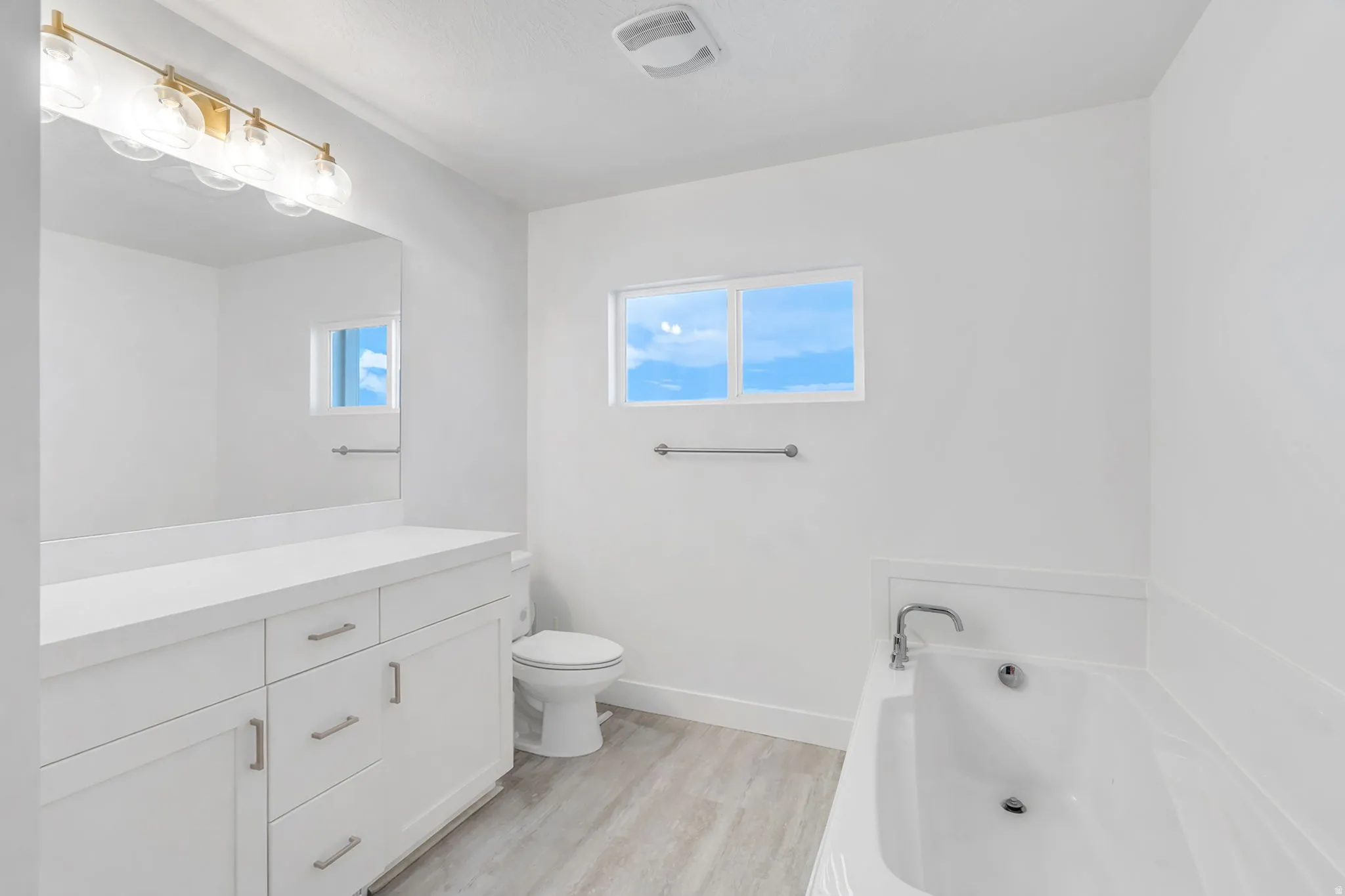 Full bath featuring light wood-style flooring, healthy amount of natural light, a bath, and vanity