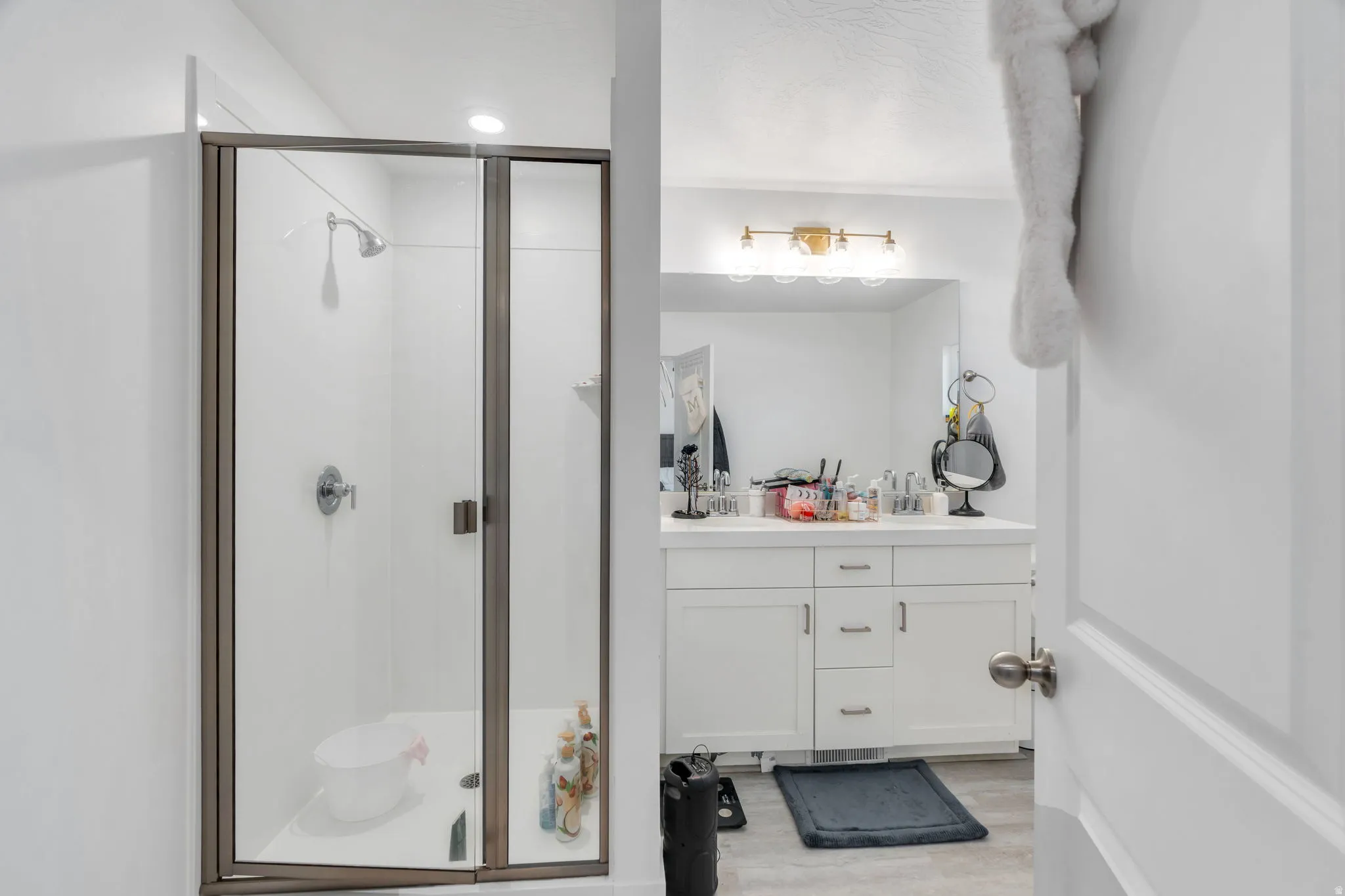 Full bath with double vanity, a stall shower, and light wood-type flooring