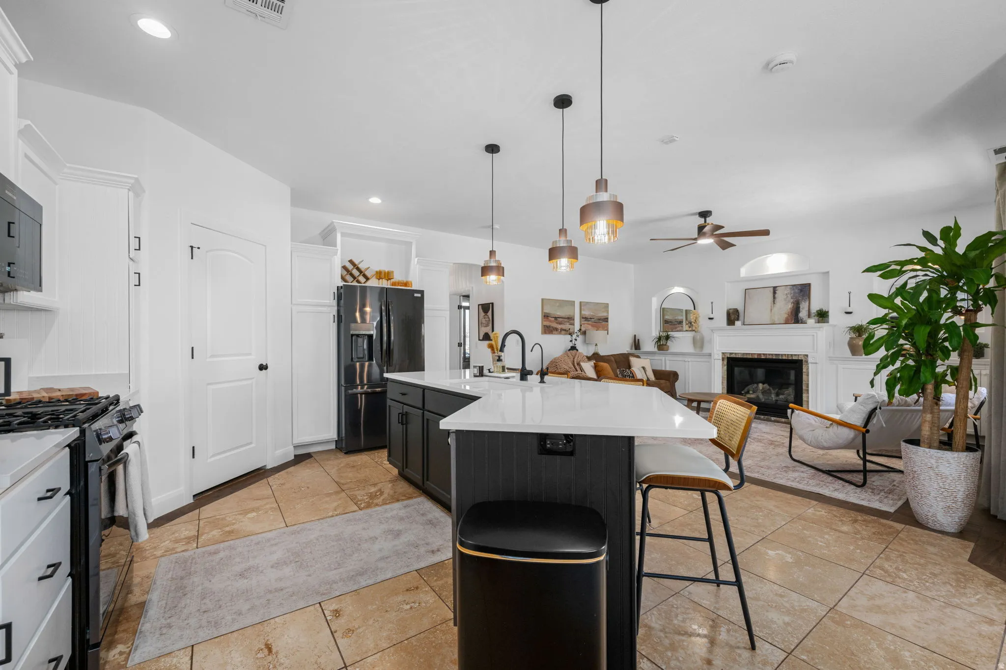 Kitchen featuring two tone cabinets, a glass covered fireplace, black appliances, open floor plan, and a breakfast bar area