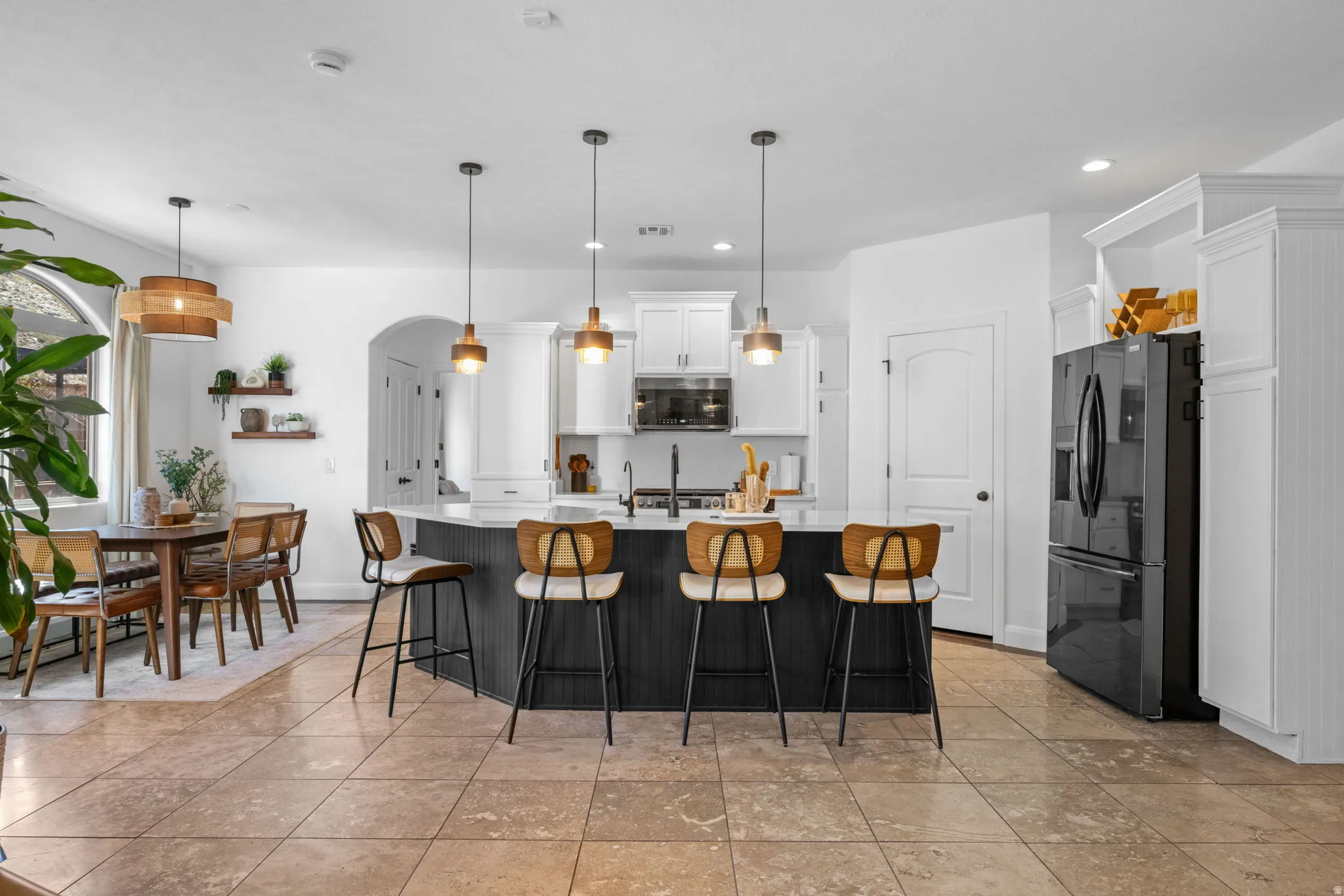 Dual tone kitchen featuring arched walkways, a breakfast bar area, fridge with ice dispenser, a kitchen island with sink, and two tone color scheme