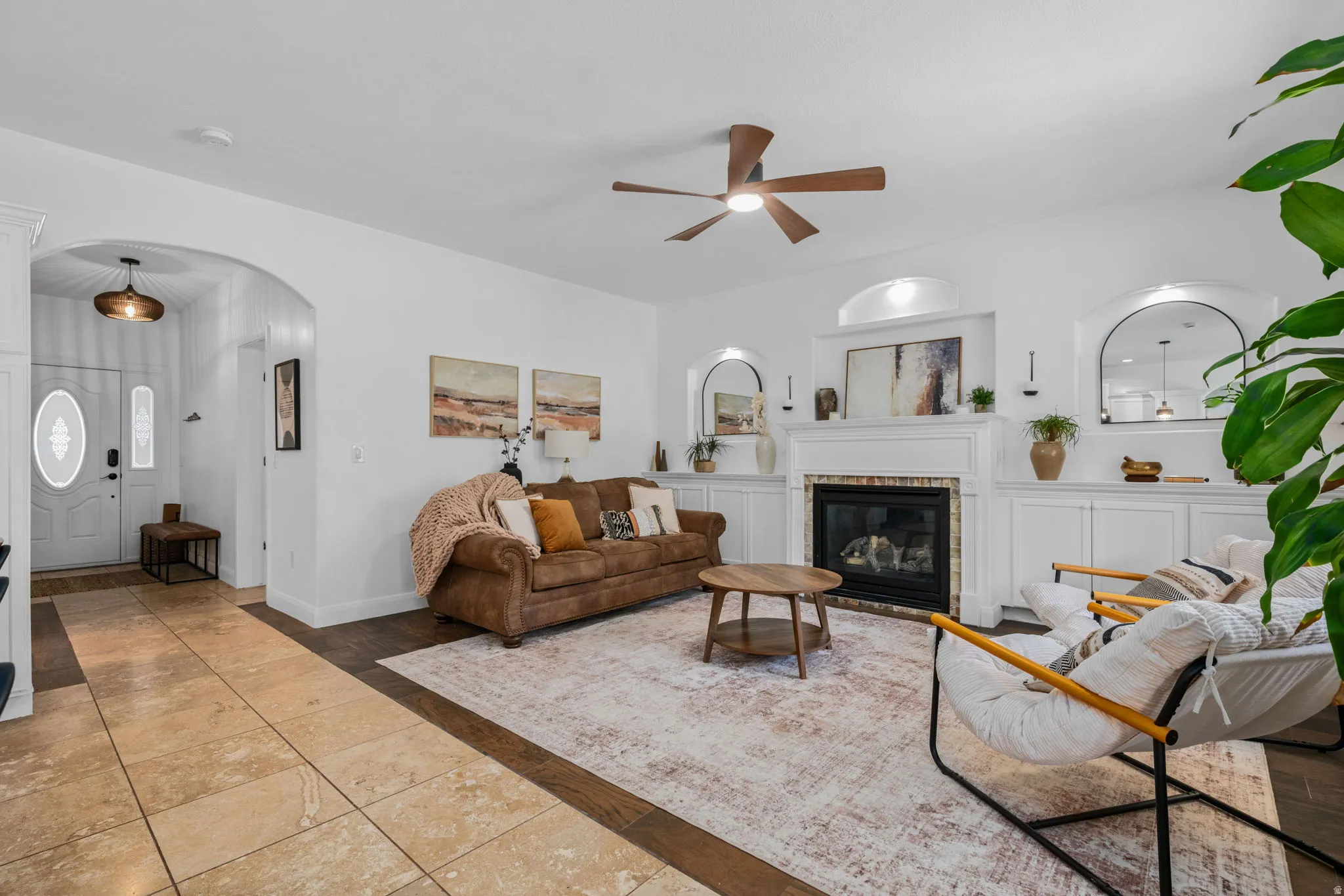 Tiled living room featuring arched walkways, a glass covered fireplace, and a ceiling fan