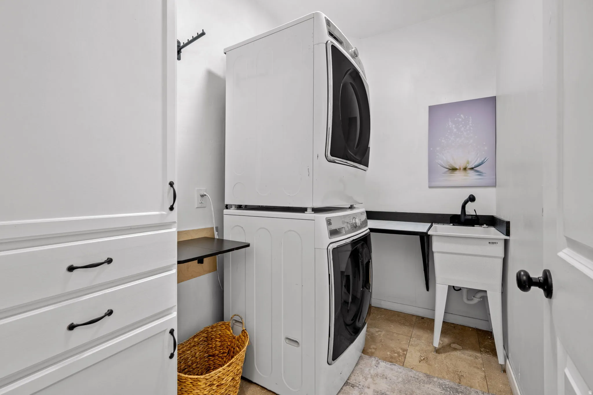 Laundry room with stacked washing machine and dryer and light stone finish floors