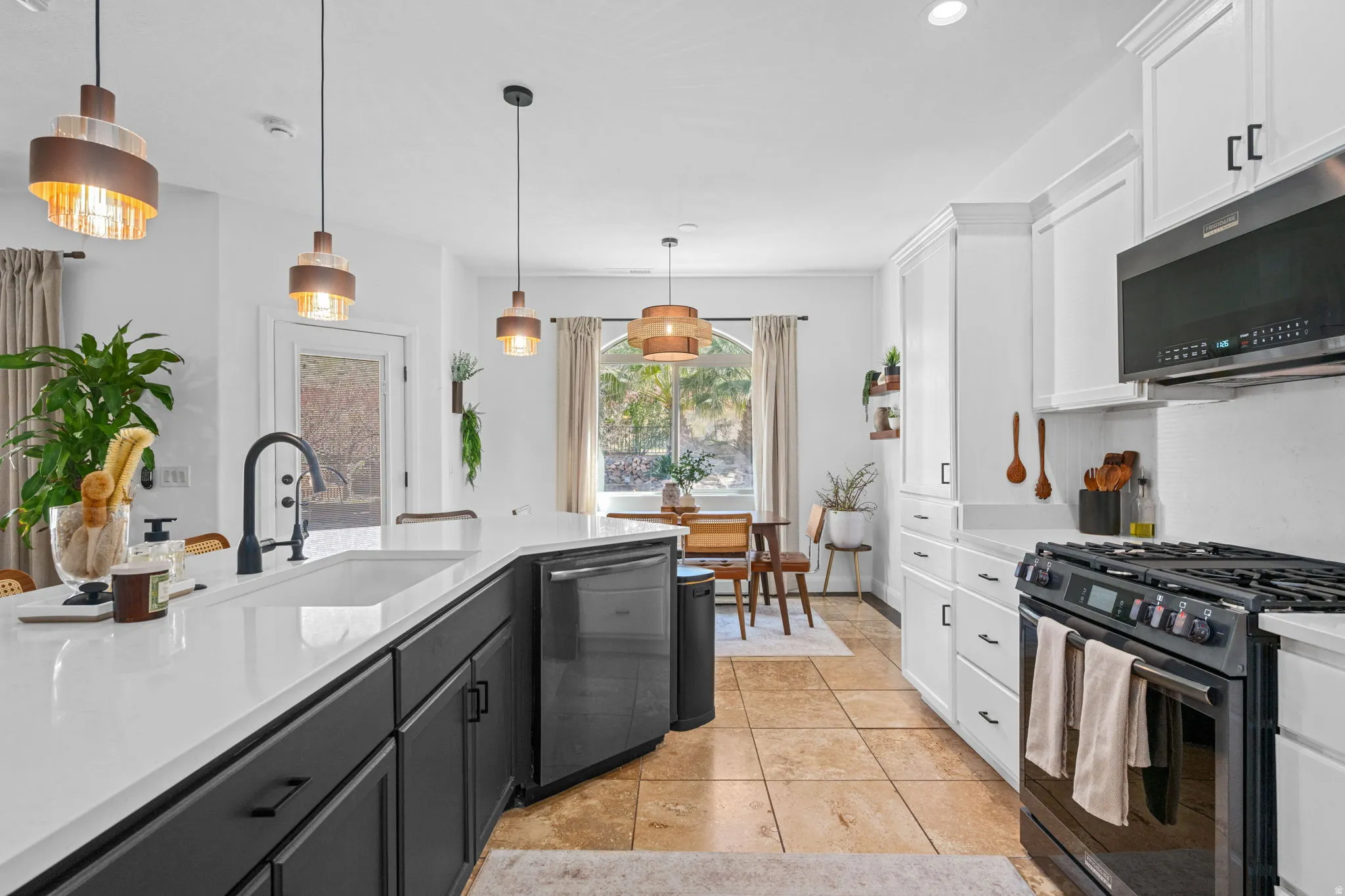 Two tone kitchen with black appliances, two tone color scheme, hanging light fixtures, light stone counters, and light tile patterned floors
