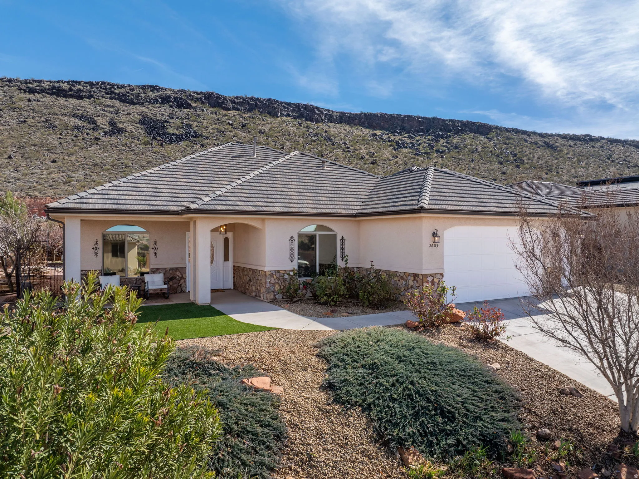 Ranch-style home featuring stone siding, an attached garage, stucco siding, a mountain view, and concrete driveway