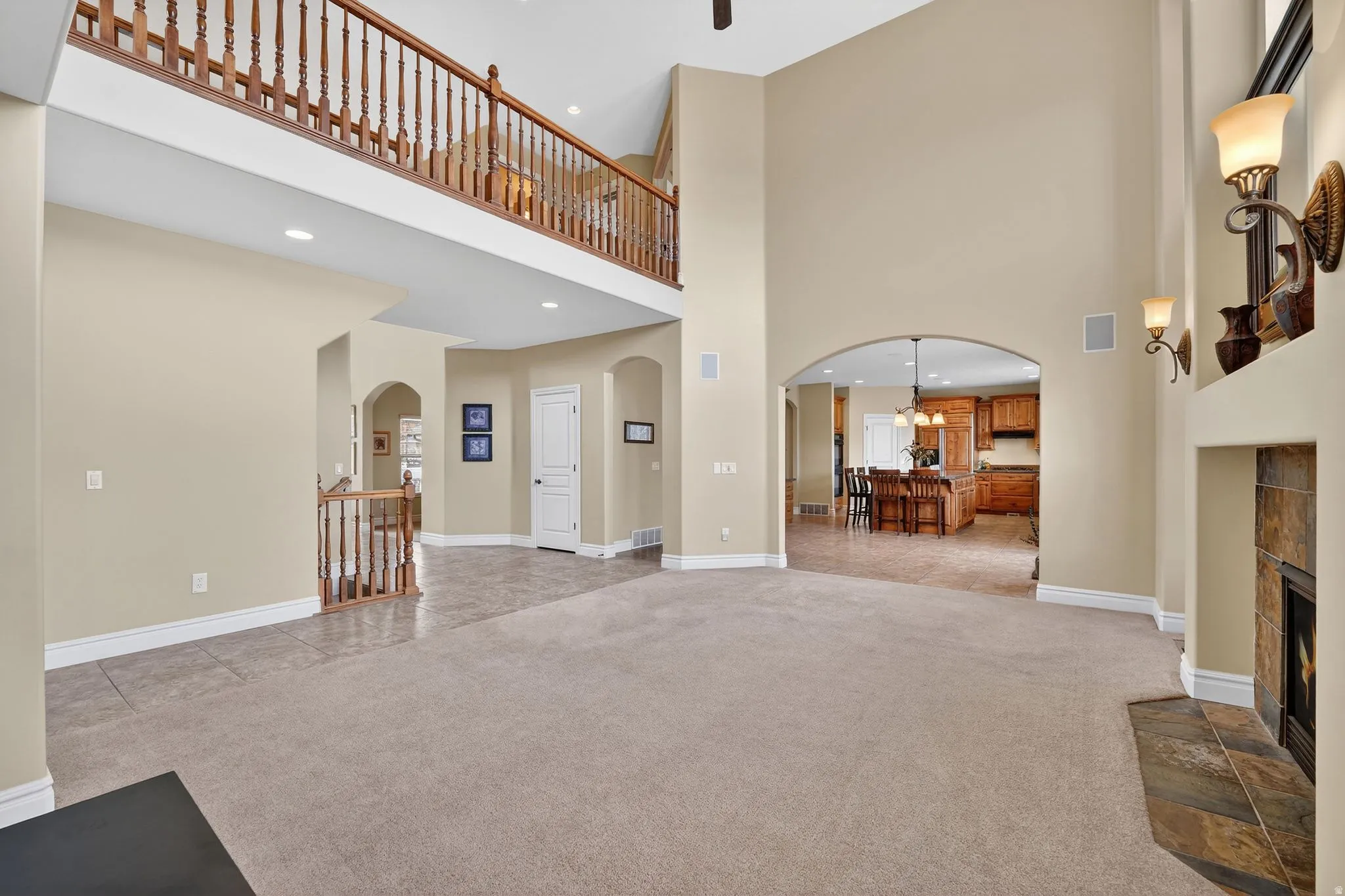 Living room featuring arched walkways, a tiled fireplace, light carpet, recessed lighting, and a high ceiling