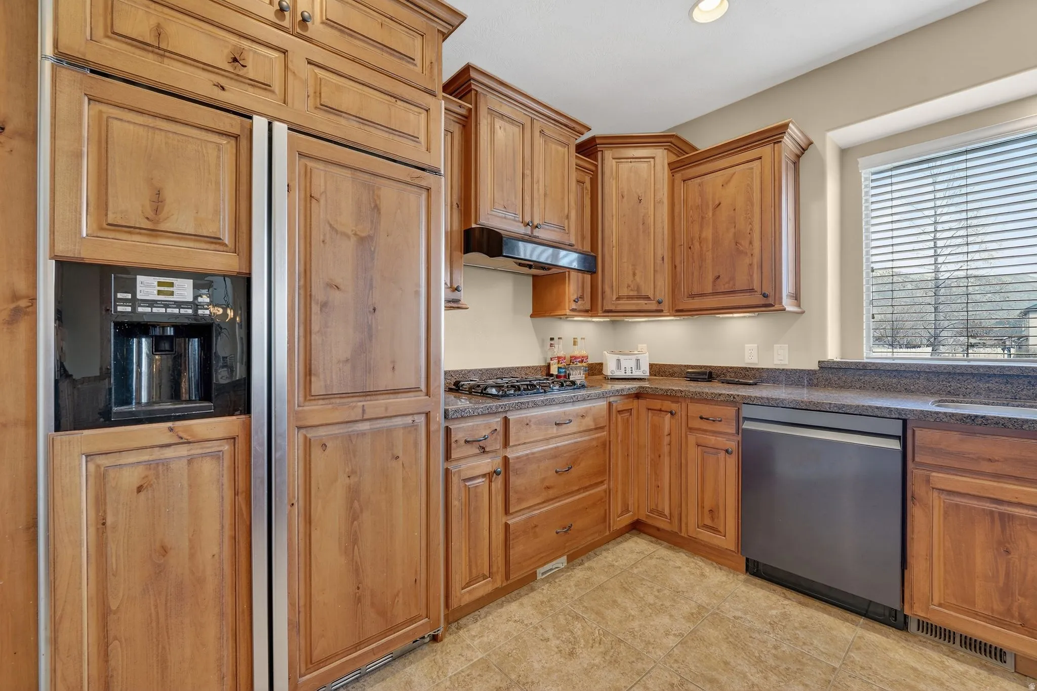 Kitchen featuring stainless steel appliances, wood finish cabinetry, recessed lighting, and dark stone countertops