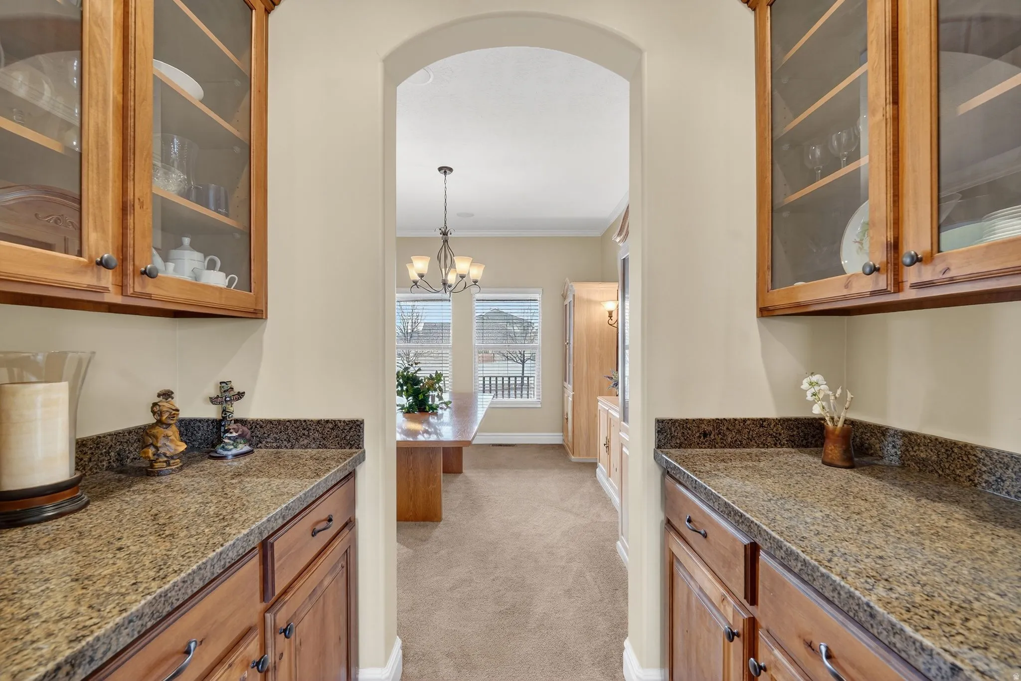 Bulters pantry  area with glass-fronted cabinets, wood finish cabinetry, arched walkways, and dark stone countertops