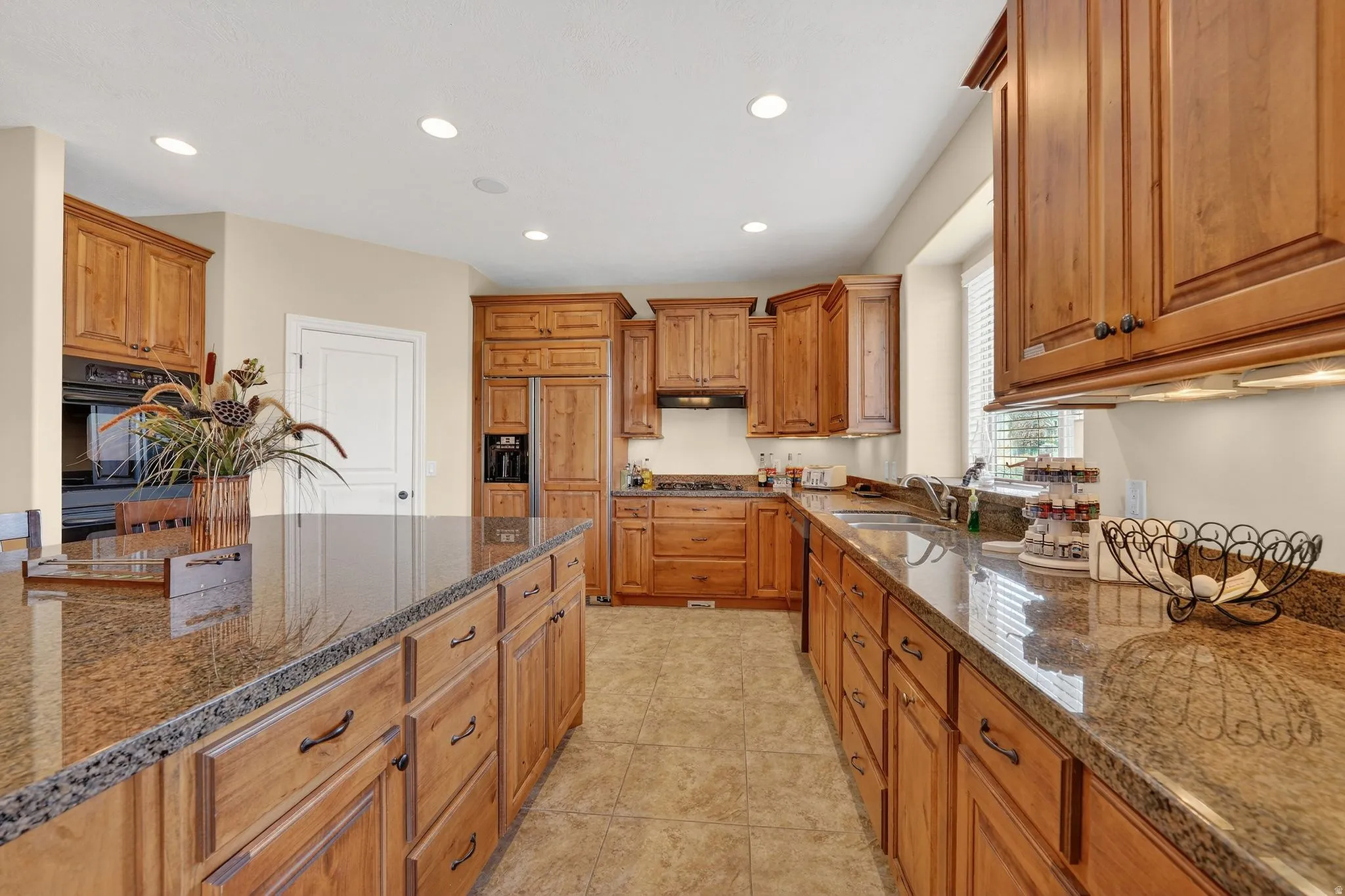 Kitchen with wood finish cabinets, dark stone countertops, stainless steel appliances, recessed lighting, and light tile patterned floors