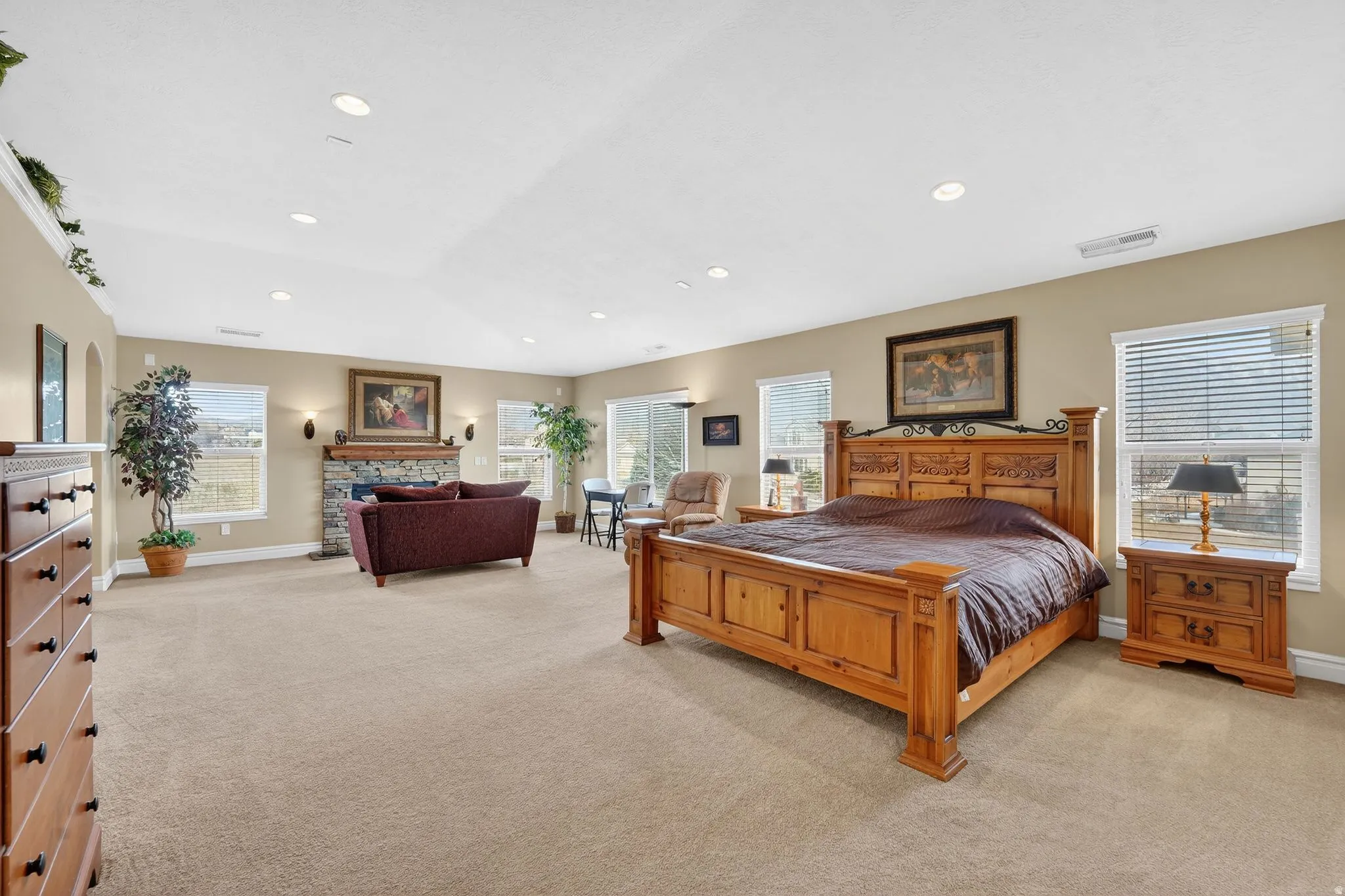 Bedroom featuring light colored carpet, a stone fireplace, recessed lighting, and vaulted ceiling