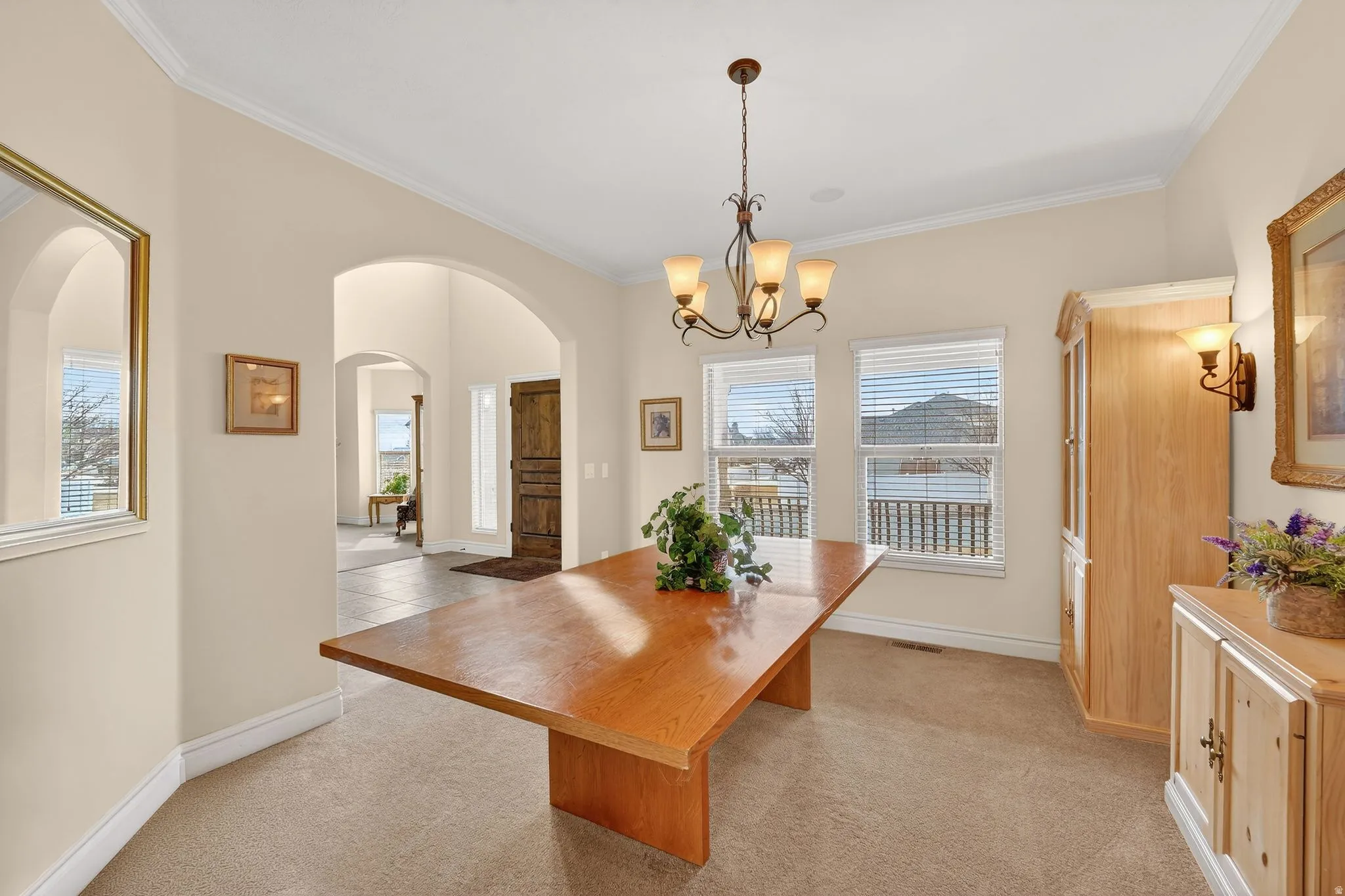 Dining area with light colored carpet, hanging lights, arched walkways, and crown molding