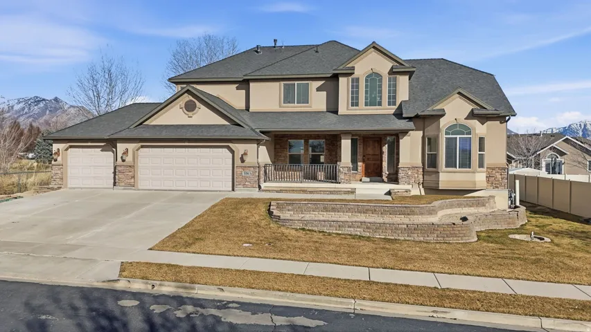 View of front facade with covered porch, stucco siding, stone siding, roof with shingles, and an attached garage