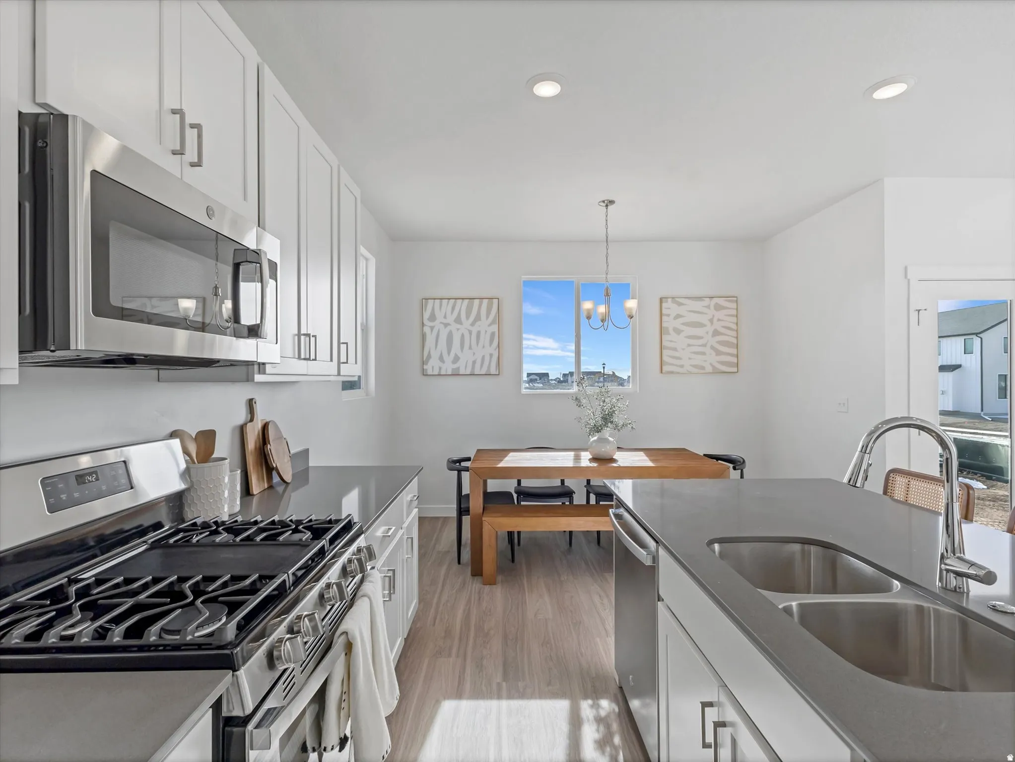 Kitchen with stainless steel appliances, white cabinetry, light wood finished floors, dark stone countertops, and hanging lights