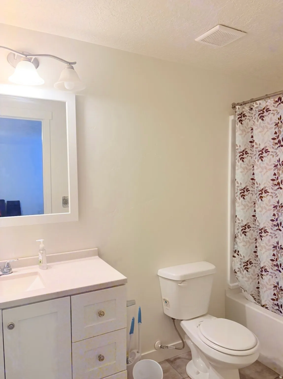 Bathroom featuring vanity, shower / tub combo, a textured ceiling, and light tile patterned flooring