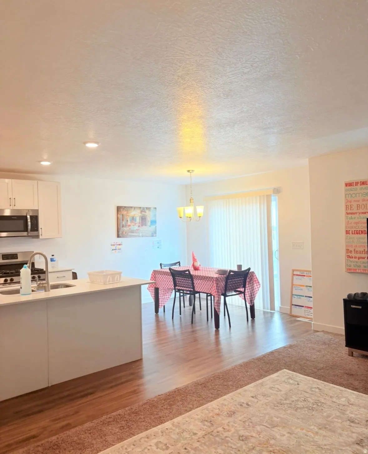 Kitchen featuring stainless steel appliances, white cabinetry, light wood-style floors, a textured ceiling, and a chandelier