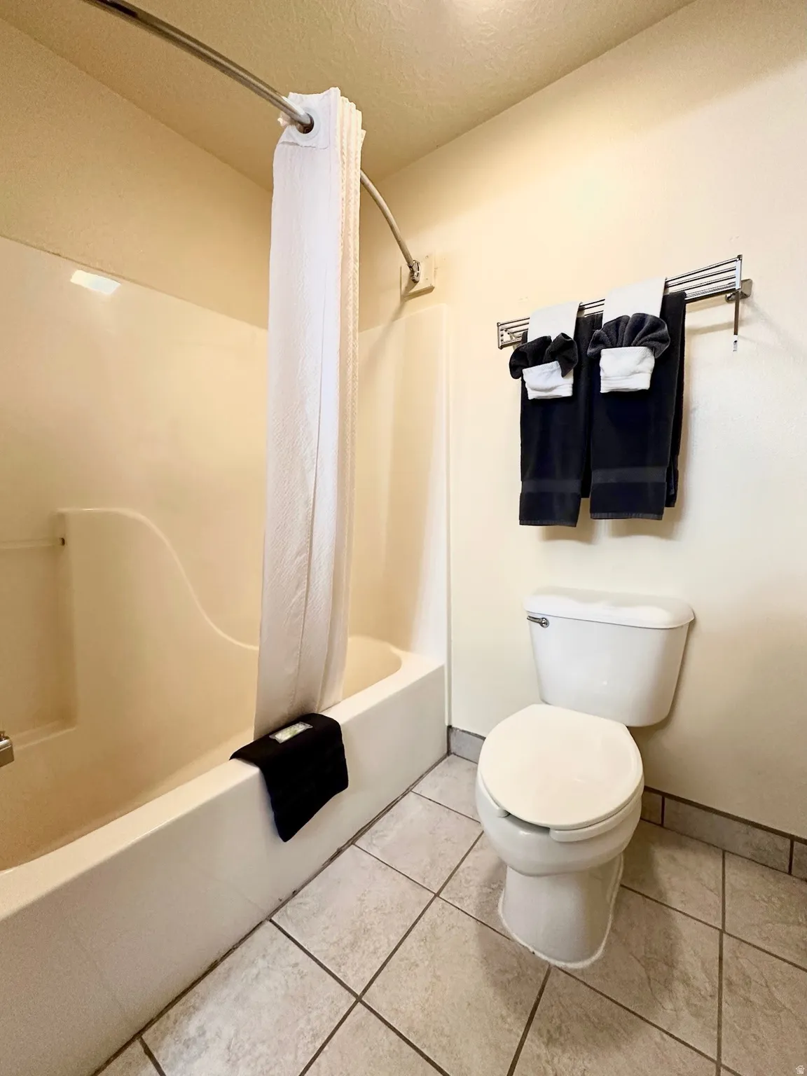Bathroom with shower / bath combination with curtain, light tile patterned floors, and a textured ceiling