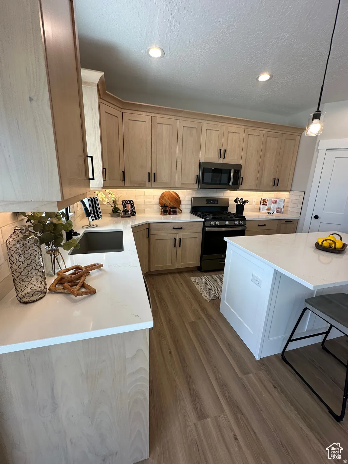 Kitchen with stainless steel appliances, light stone countertops, hanging light fixtures, a kitchen breakfast bar, and dark wood finished floors