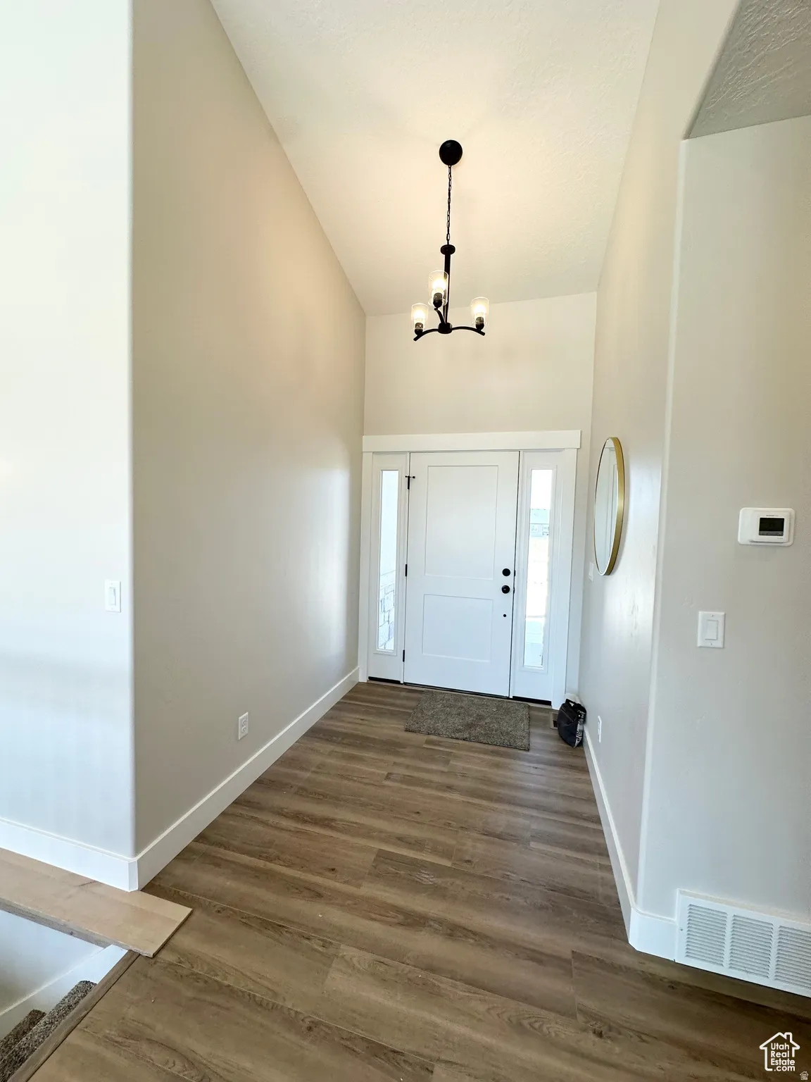 Foyer entrance with vaulted ceiling, dark wood finished floors, and a chandelier
