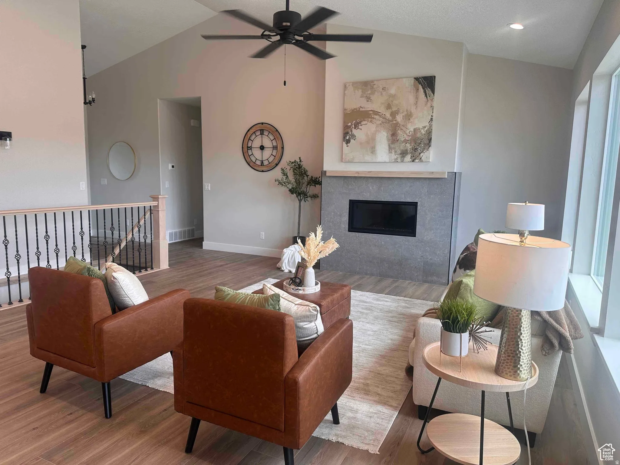 Living area with lofted ceiling, wood finished floors, a glass covered fireplace, and ceiling fan