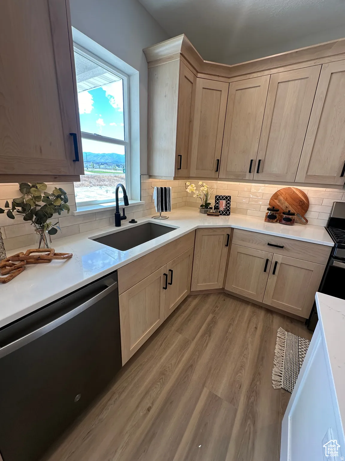 Kitchen featuring dishwasher, light wood finished floors, decorative backsplash, light stone counters, and stove