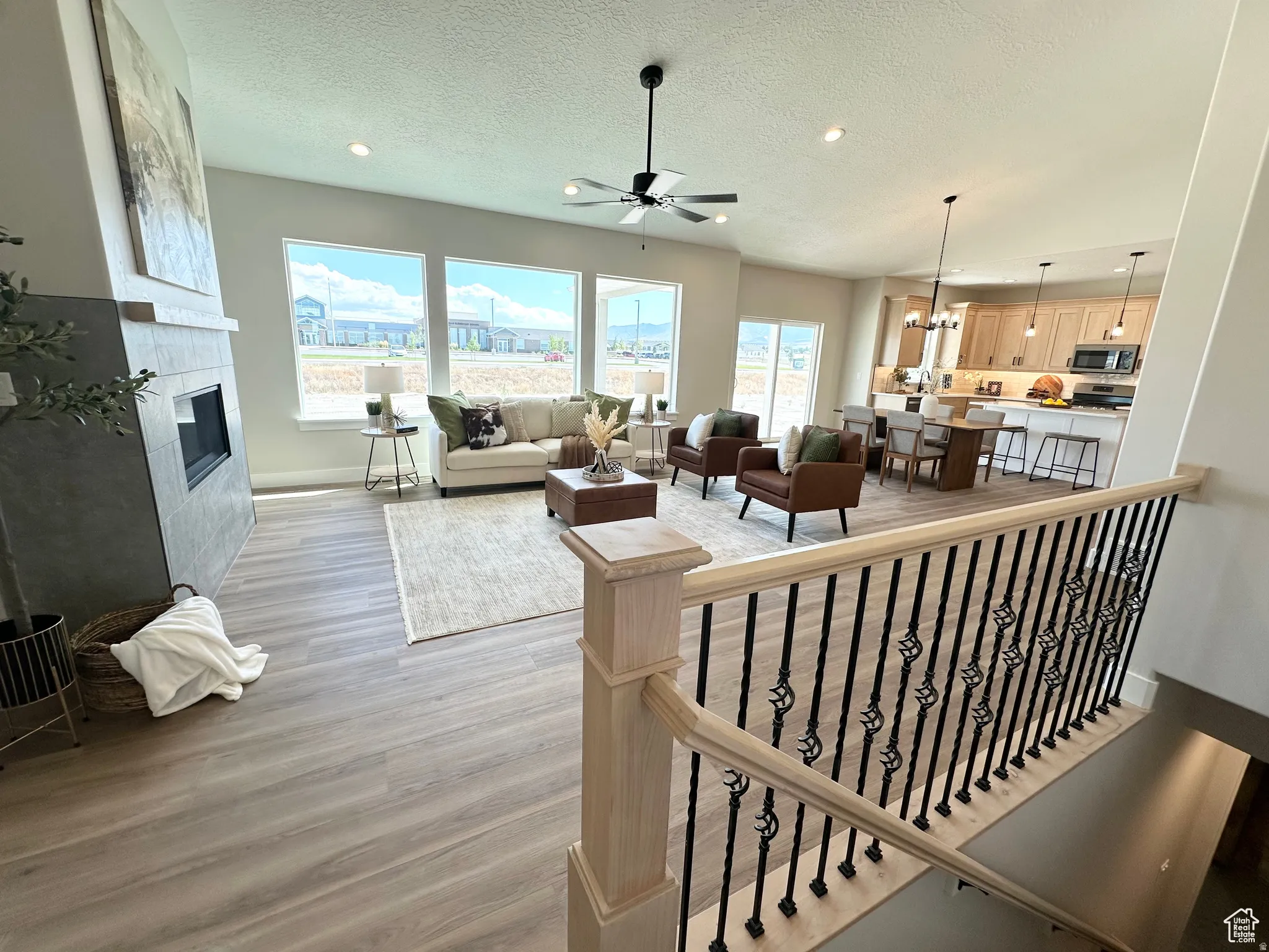 Living room with ceiling fan, a chandelier, a textured ceiling, light wood-type flooring, and a fireplace