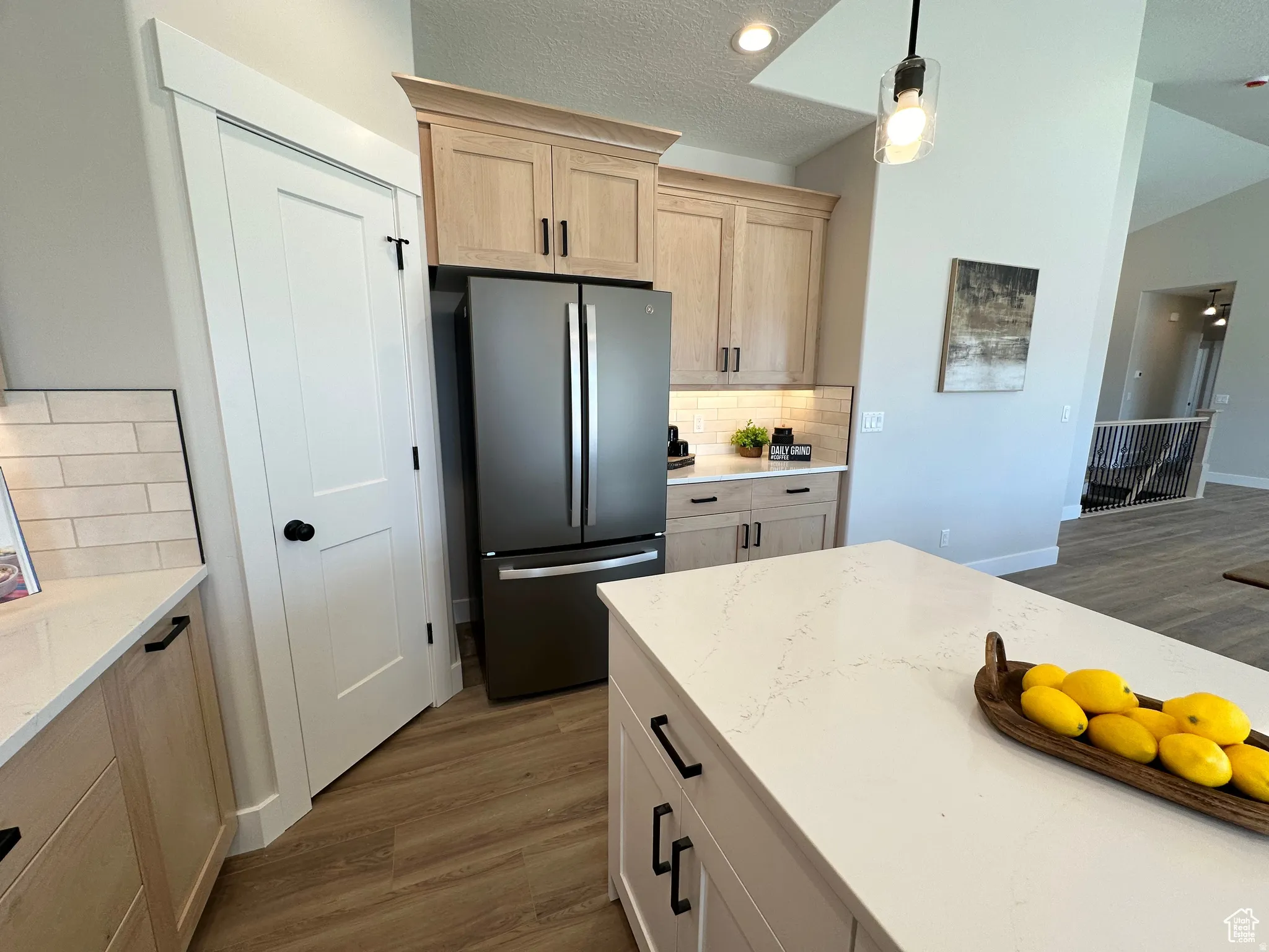 Kitchen with dark wood finished floors, light wood finish cabinetry, backsplash, freestanding refrigerator, and light stone countertops