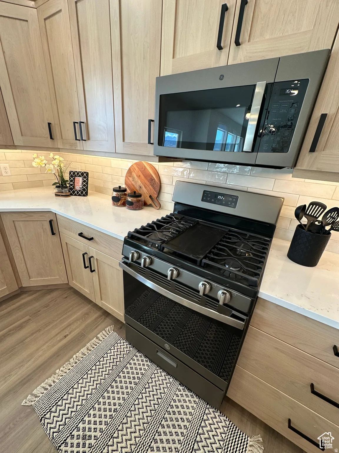 Kitchen featuring stainless steel appliances, light wood finish cabinets, light stone countertops, decorative backsplash, and light wood-type flooring