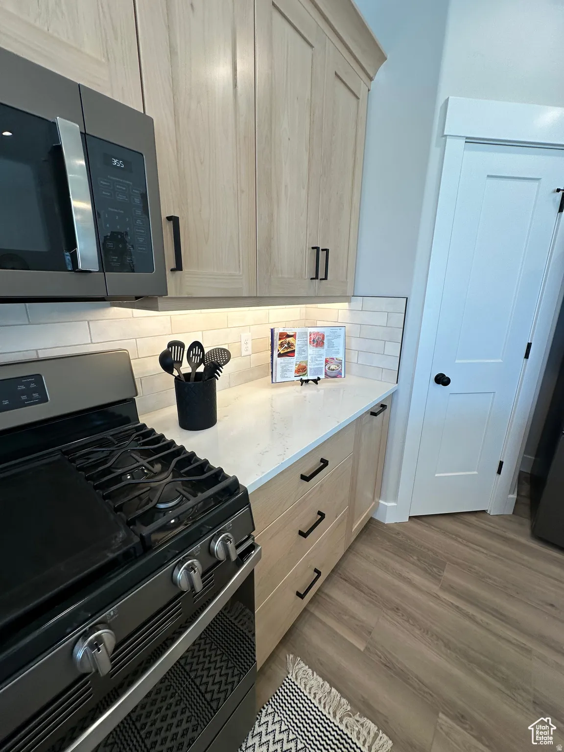 Kitchen with range with gas stovetop, stainless steel microwave, light wood finish cabinets, light stone countertops, and light wood-style floors
