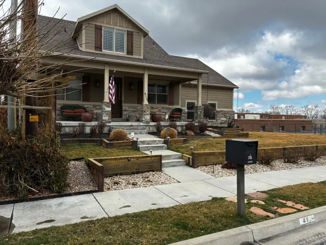 View of front of property featuring covered porch, a shingled roof, board and batten siding, a front yard, and stone siding