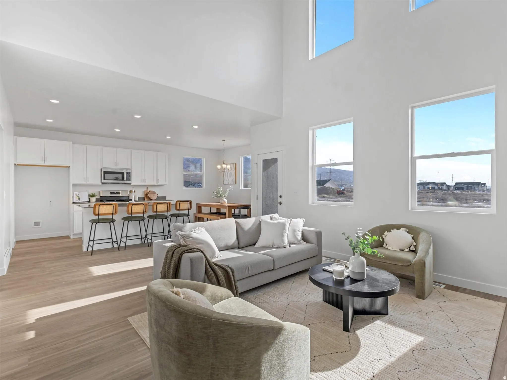 Living room with light wood finished floors, suspended lighting, and a high ceiling