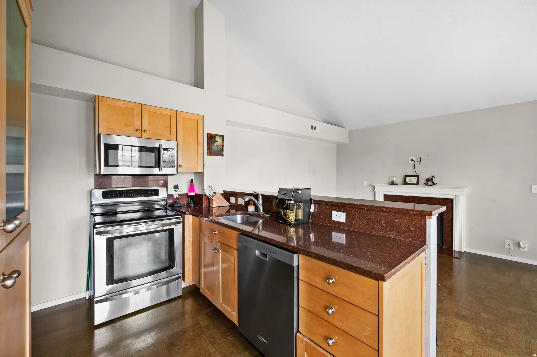 Kitchen featuring a peninsula, stainless steel appliances, vaulted ceiling, and dark stone counters