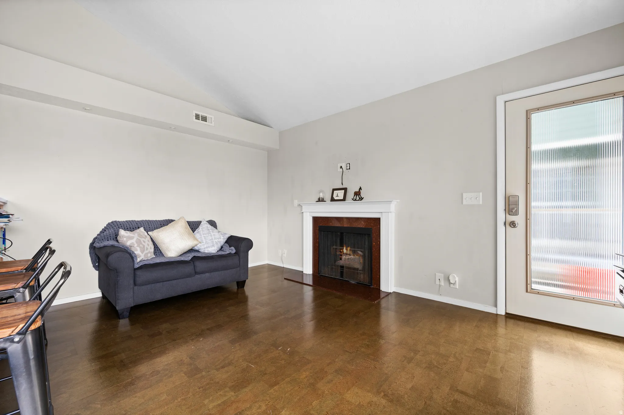 Sitting room featuring vaulted ceiling, dark wood-type flooring, and a warm lit fireplace