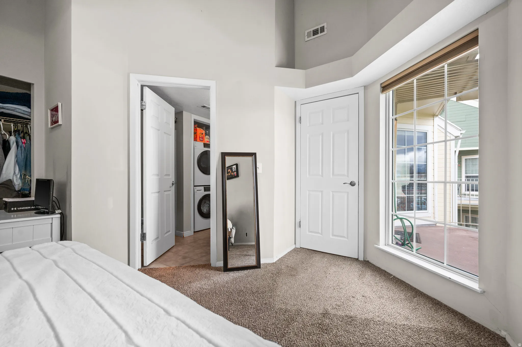 Bedroom featuring a closet, light carpet, stacked washing machine and dryer, and a high ceiling