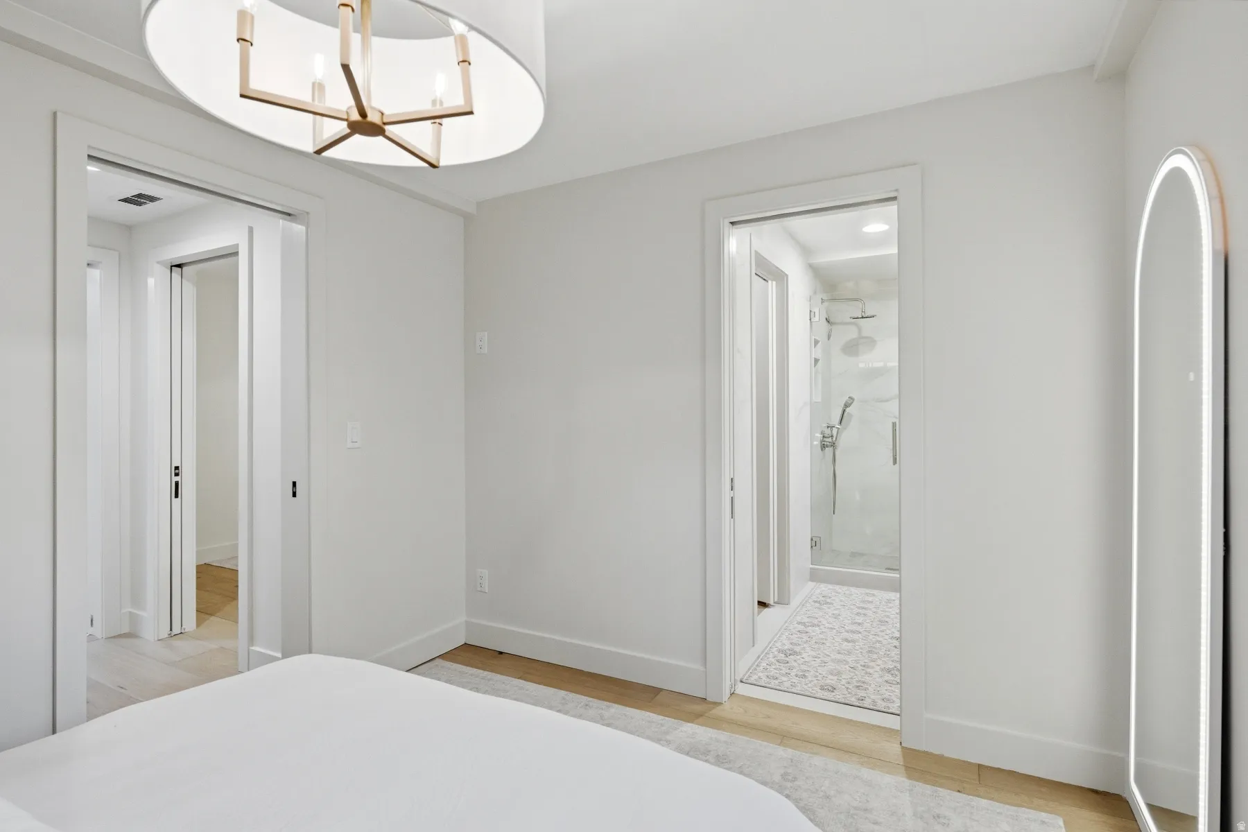 Bedroom with hanging lights, light wood-type flooring, and ensuite bath