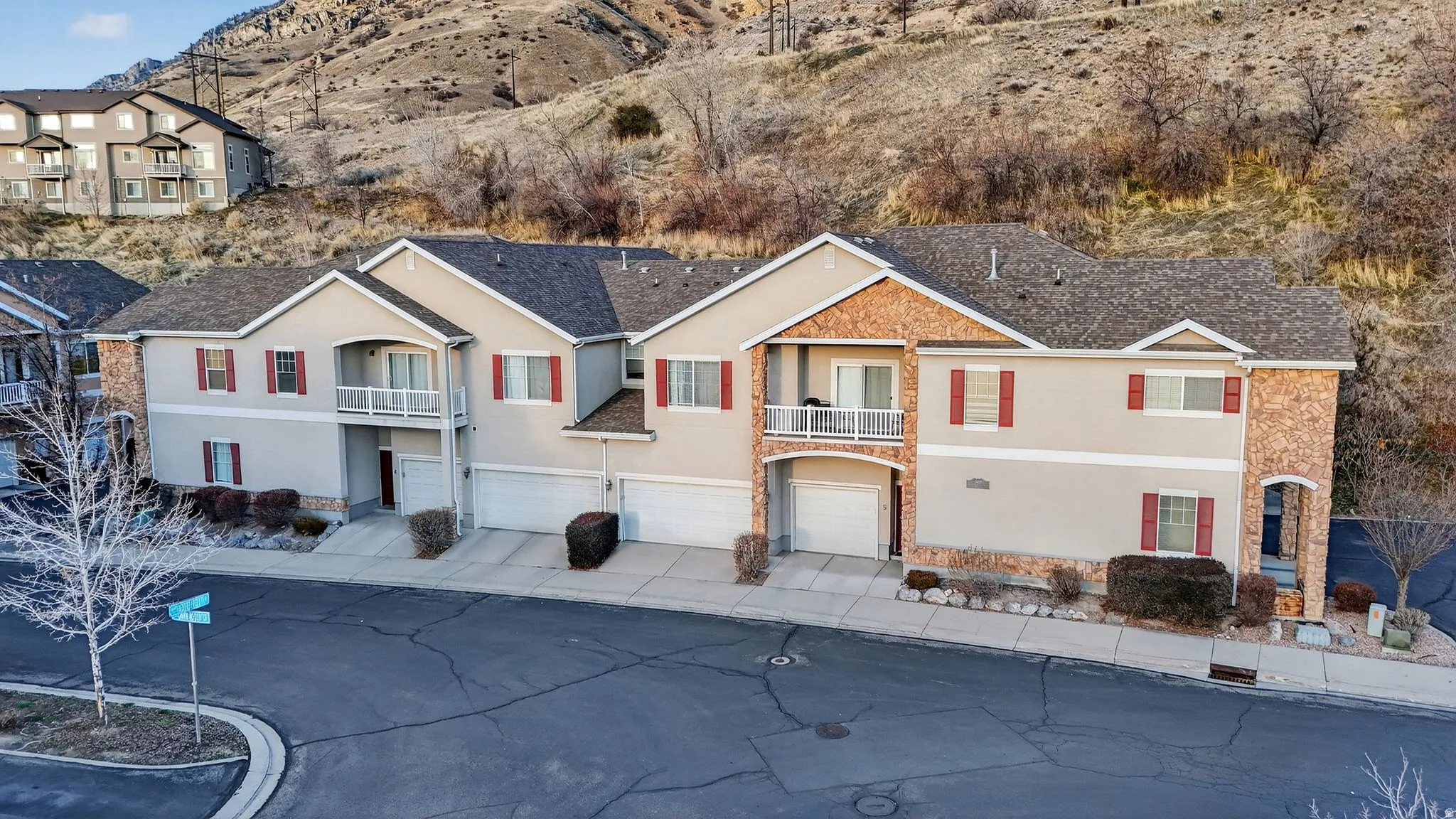 View of front facade featuring a balcony, a garage, stucco siding, driveway, and stone siding