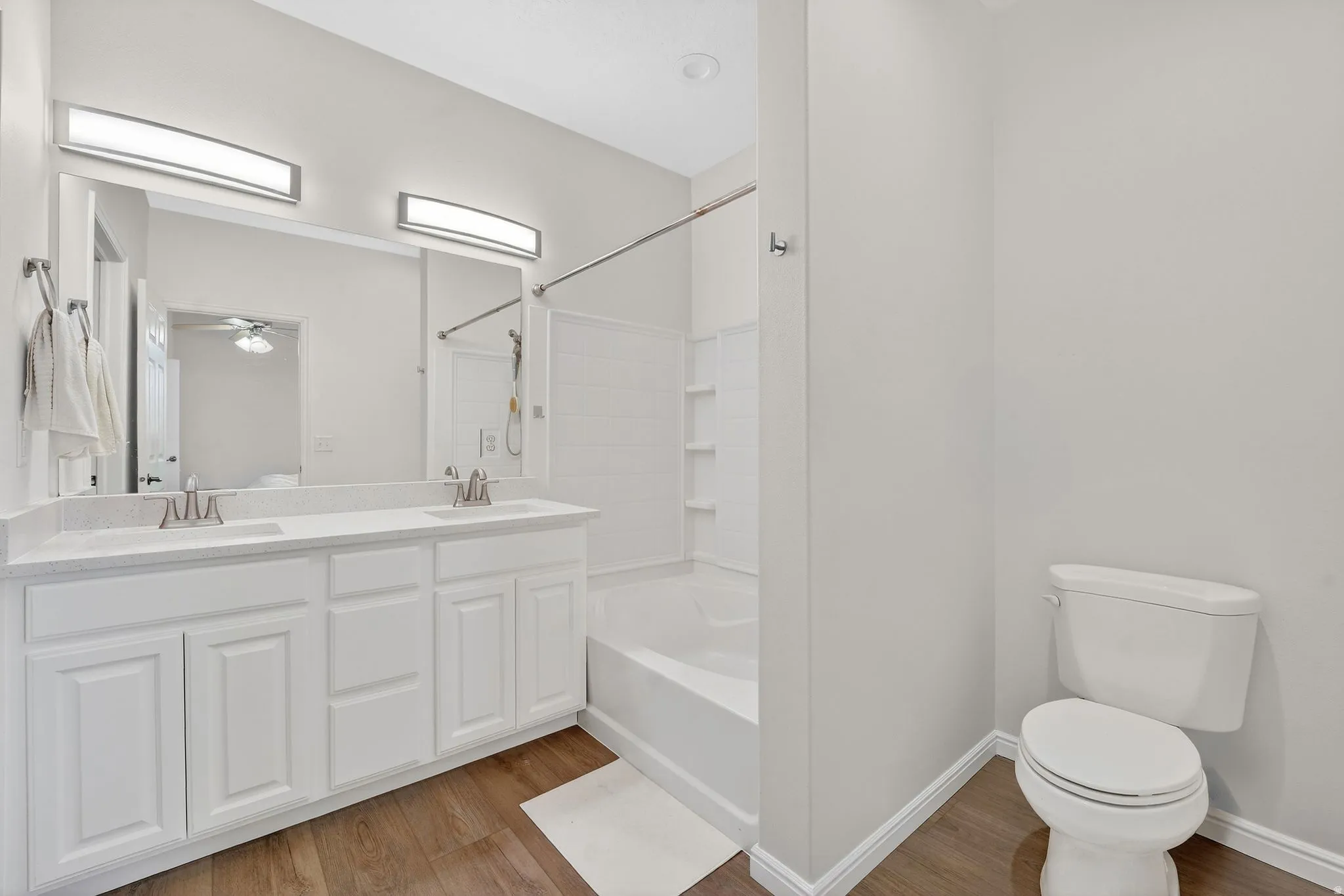 Bathroom with double vanity, light wood-style flooring, ceiling fan, and shower / bath combination