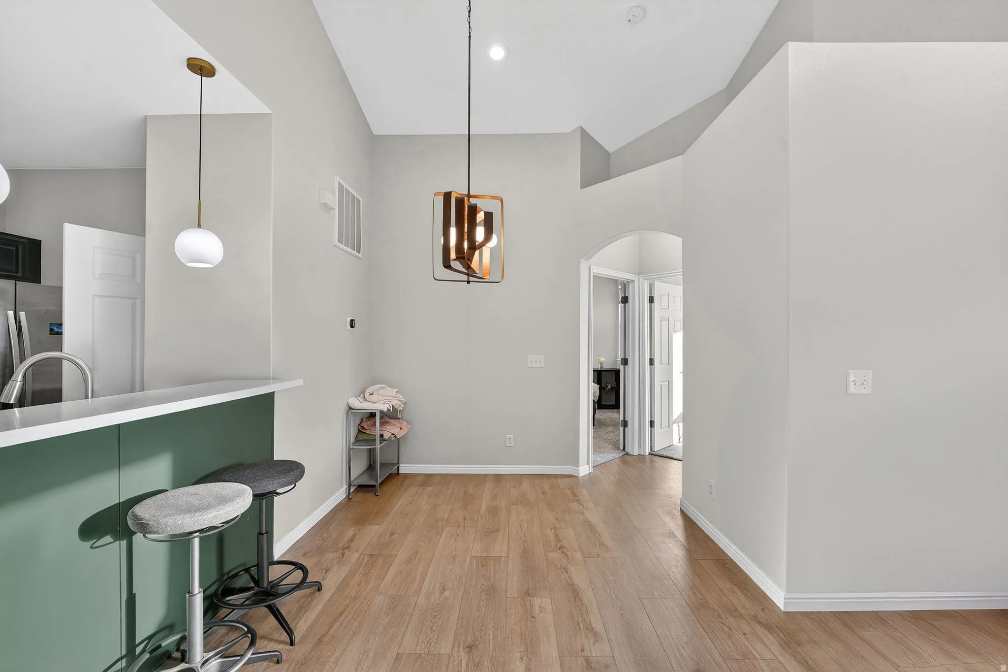 Dining area with arched walkways, light wood finished floors, lofted ceiling, and suspended lighting