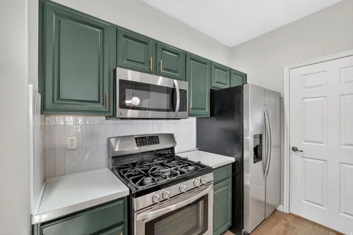 Kitchen featuring green cabinets, stainless steel appliances, light countertops, light wood-style flooring, and decorative backsplash
