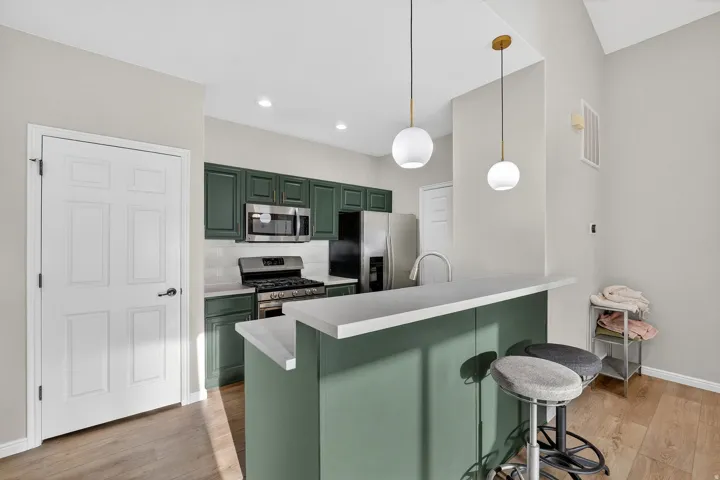 Kitchen featuring green cabinetry, a breakfast bar area, stainless steel appliances, and light countertops
